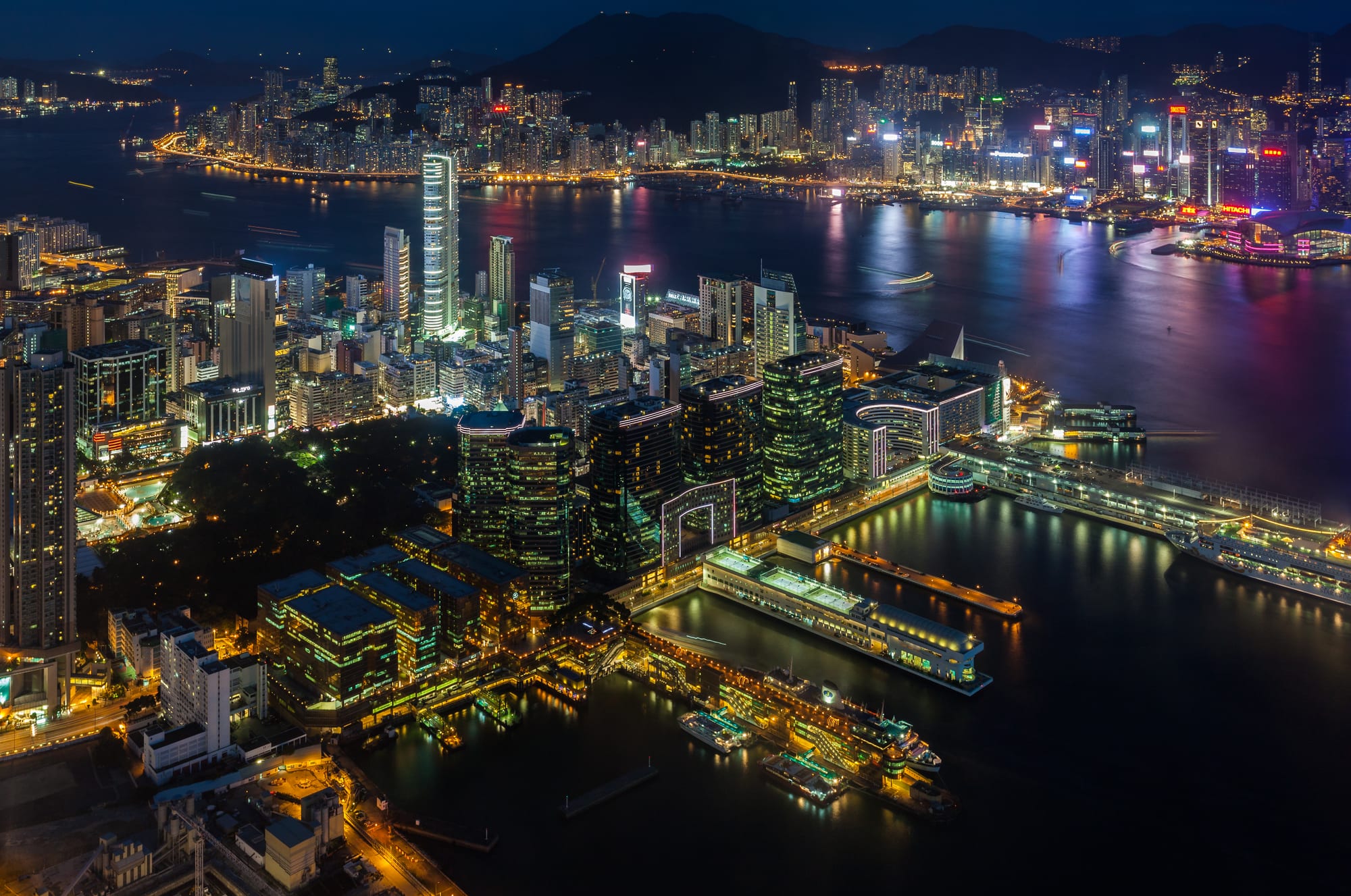 A dense wall of skyscrapers along Victoria Harbour with green mountains rising behind