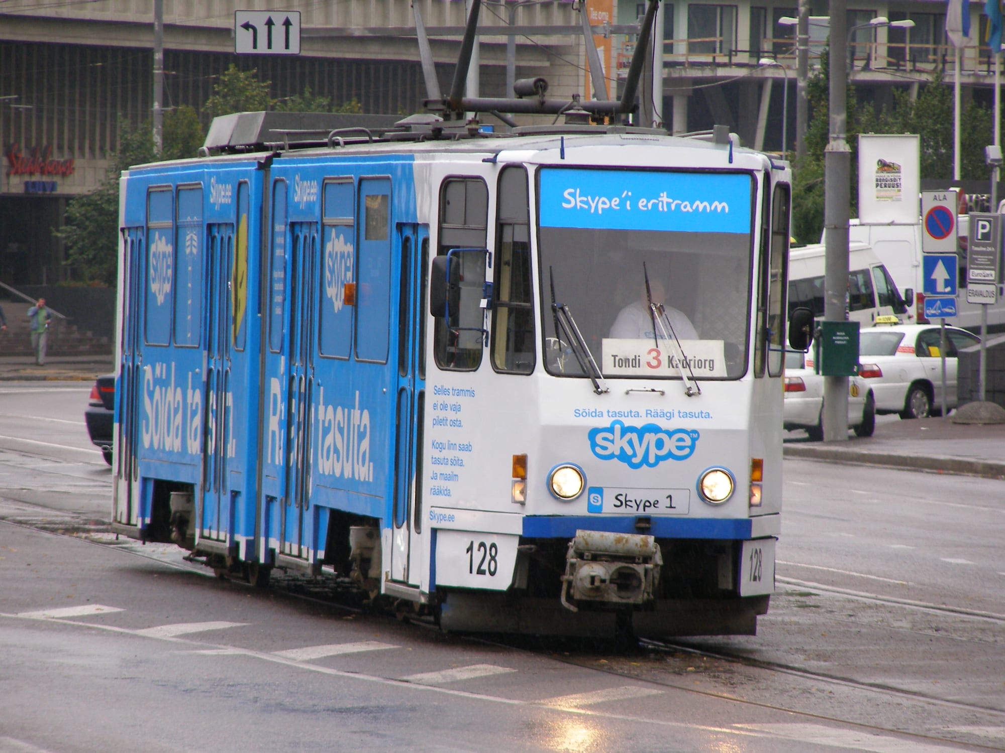 A blue and white tram covered in Skype logos and Estonian slogans on a wet city street