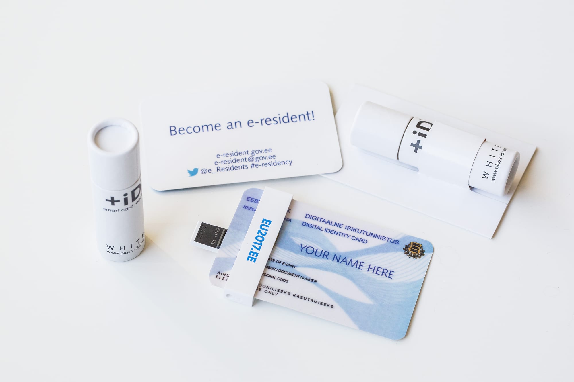 A sample Estonian digital identity card slotted into a small white USB card reader, beside a card inviting people to become an e-resident