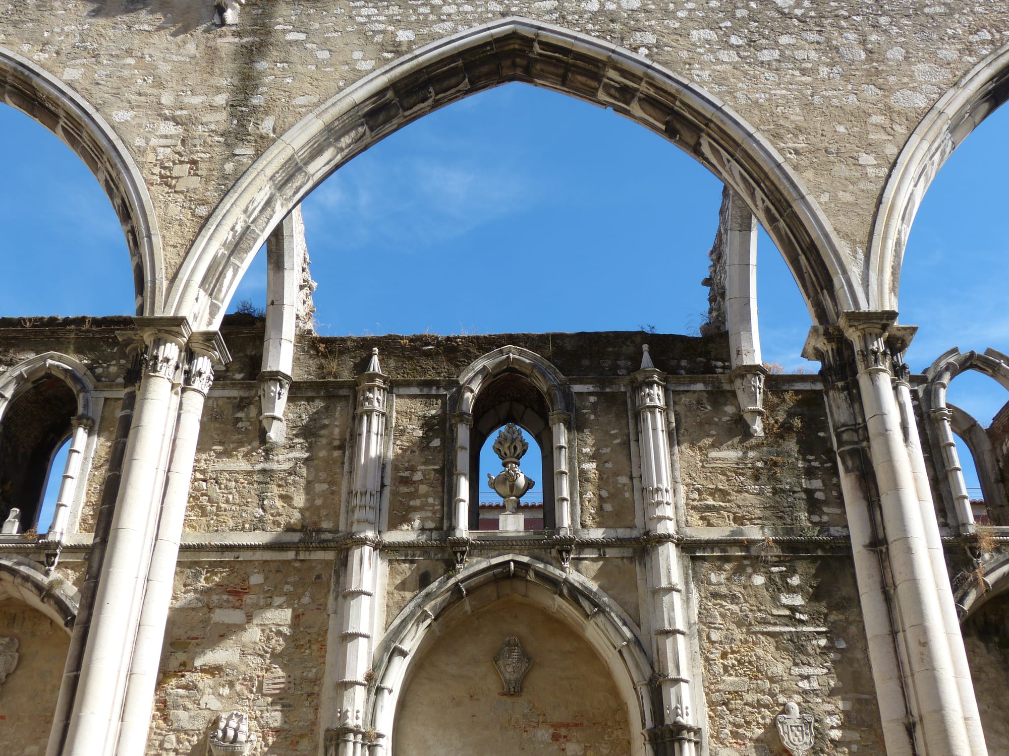 Tall pointed Gothic stone arches stand open to a bright blue sky above the ruined walls of a church nave