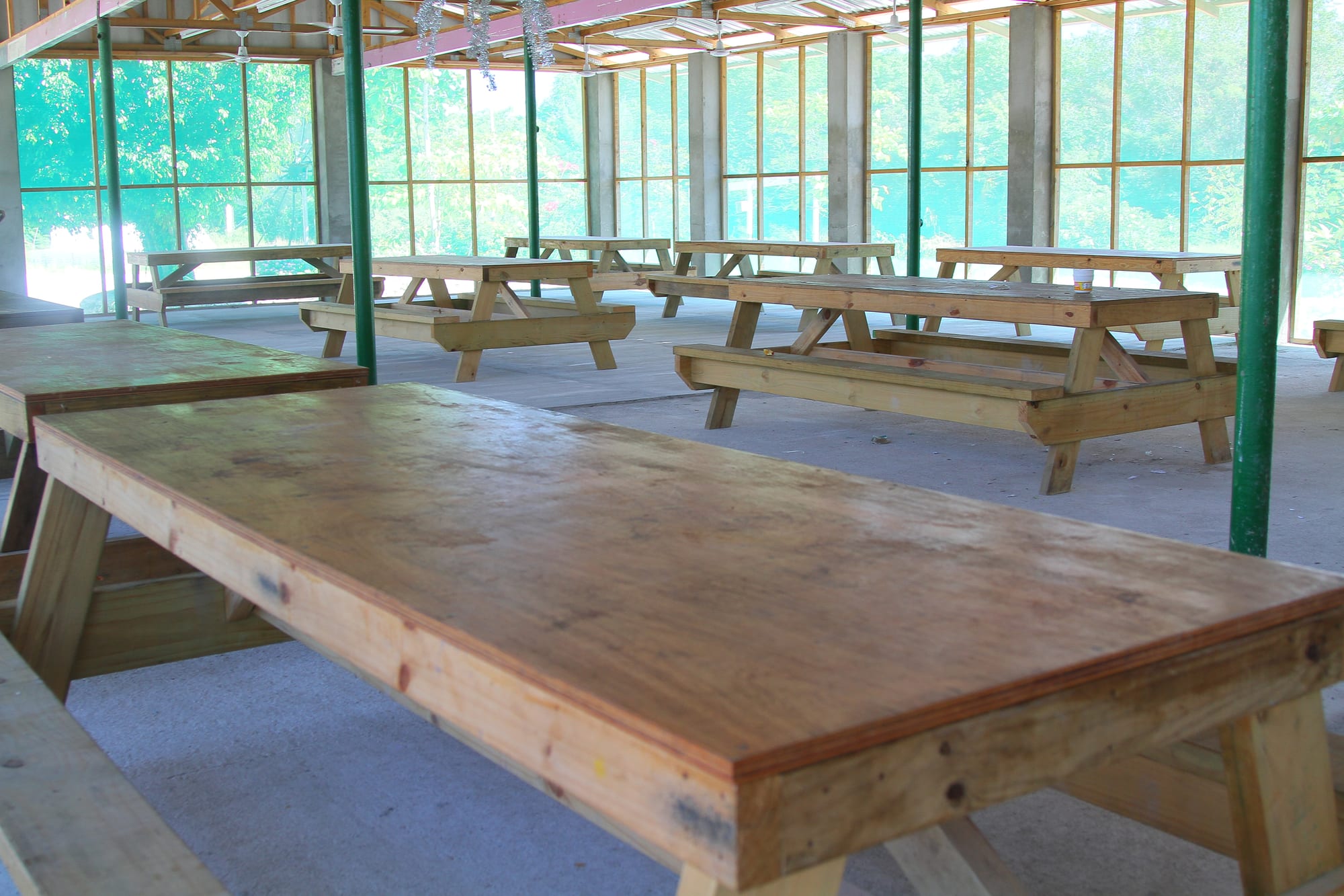 Rows of empty wooden picnic tables in an open-sided hall with screened walls
