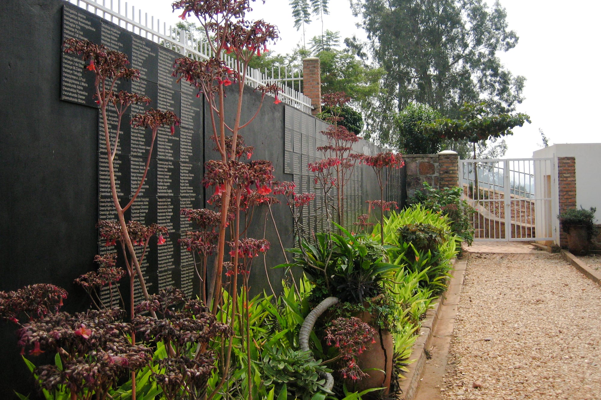 A long black wall covered with engraved panels of names, beside a garden path lined with flowering plants
