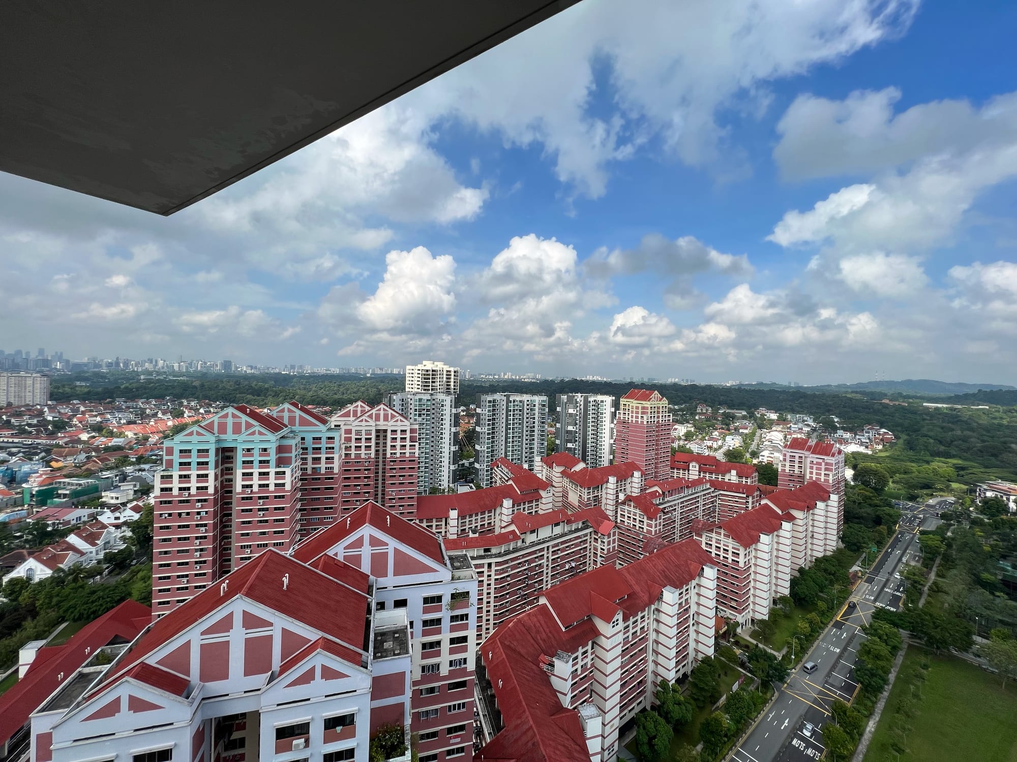 Red-roofed apartment blocks of a housing estate seen from above, with forest and distant towers beyond