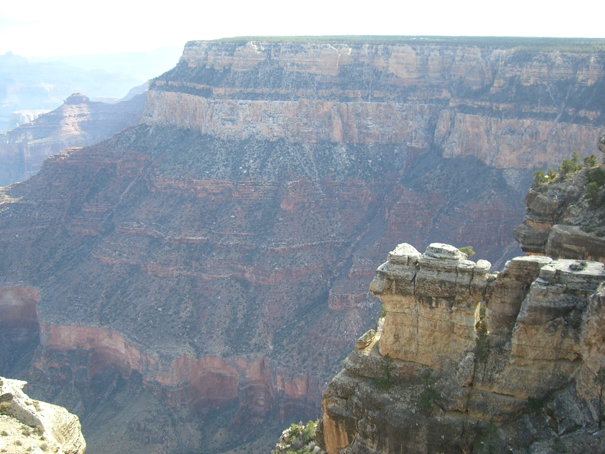 A massive canyon wall of horizontal bands: pale cliffs at the top, then red, ledged slopes, then a red-stained cliff lower down
