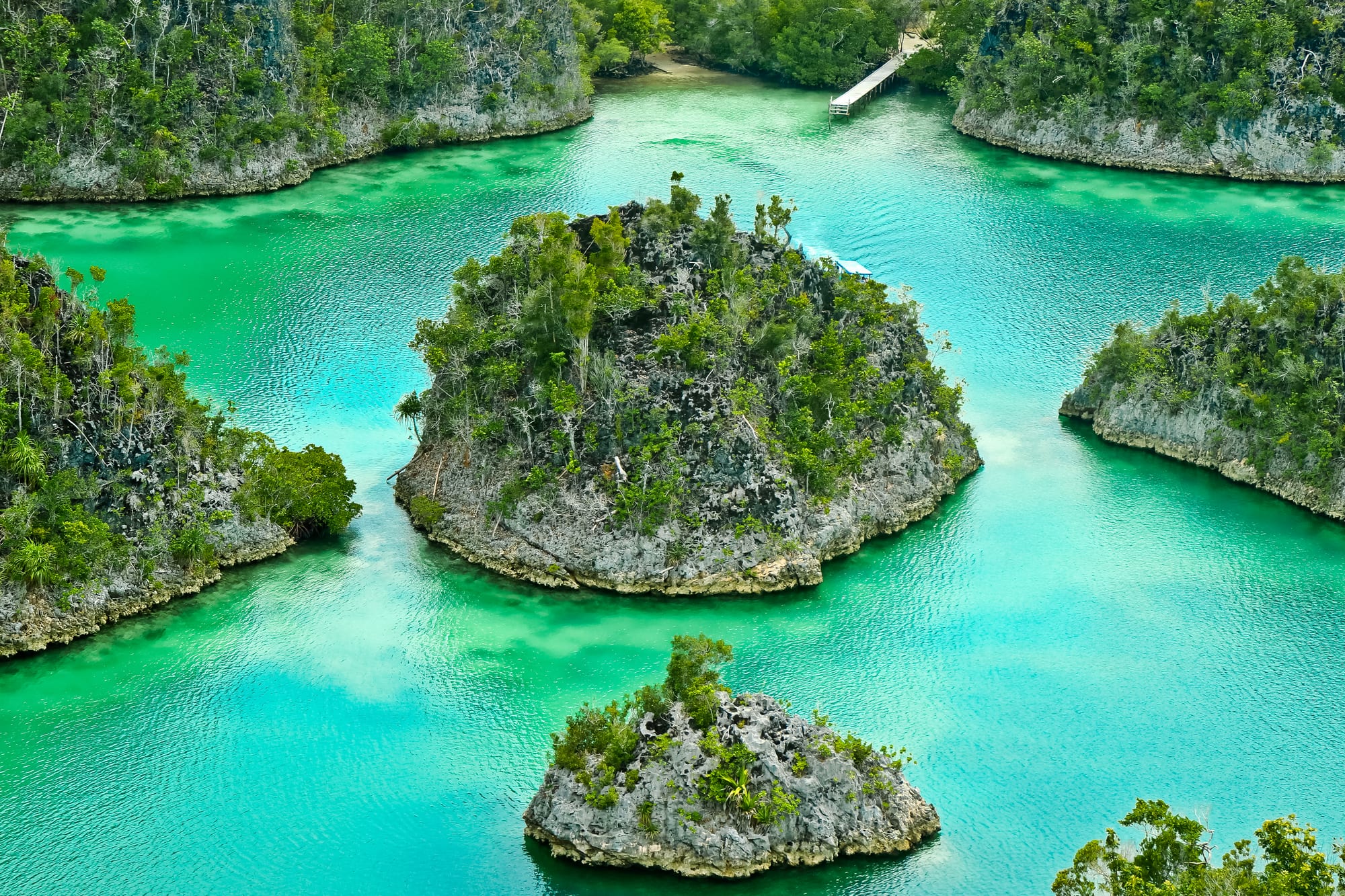 Small rocky islands covered in green forest rising from a turquoise lagoon, with a wooden jetty in the distance