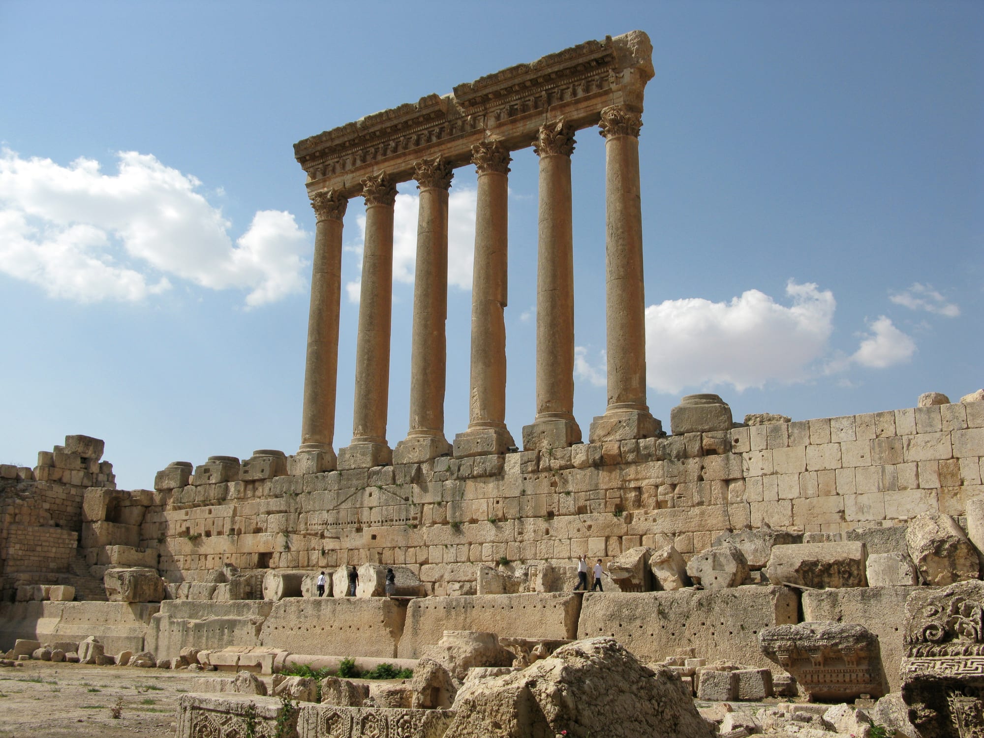 Six tall Corinthian columns carrying a carved stone entablature, standing on a stone platform against a blue sky with white clouds