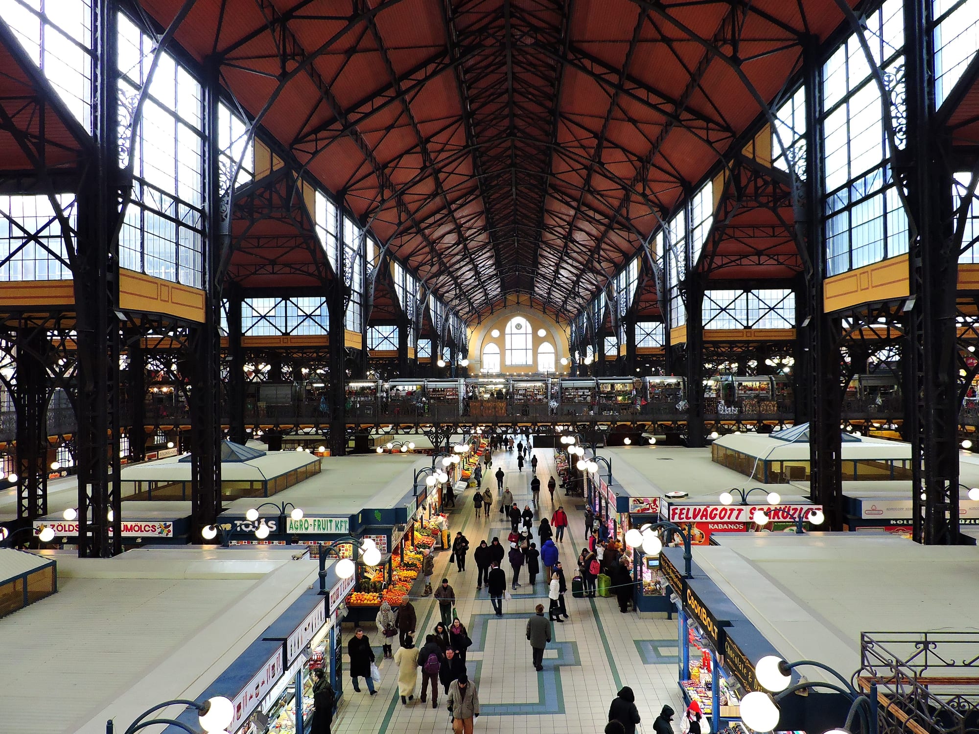 The vast iron-framed interior of a market hall in Budapest, with shoppers walking between stalls selling fruit and vegetables
