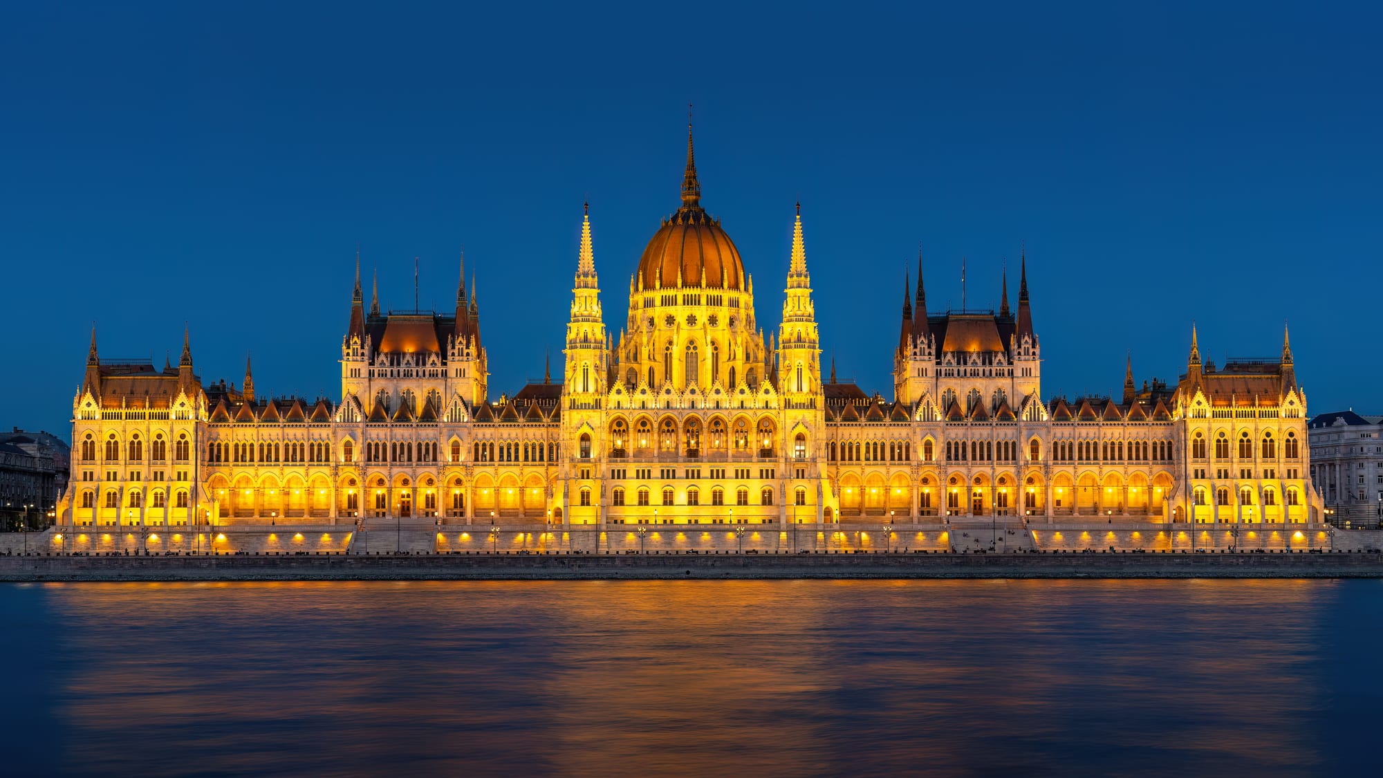 A vast neo-Gothic parliament building with a central dome and many spires along a river