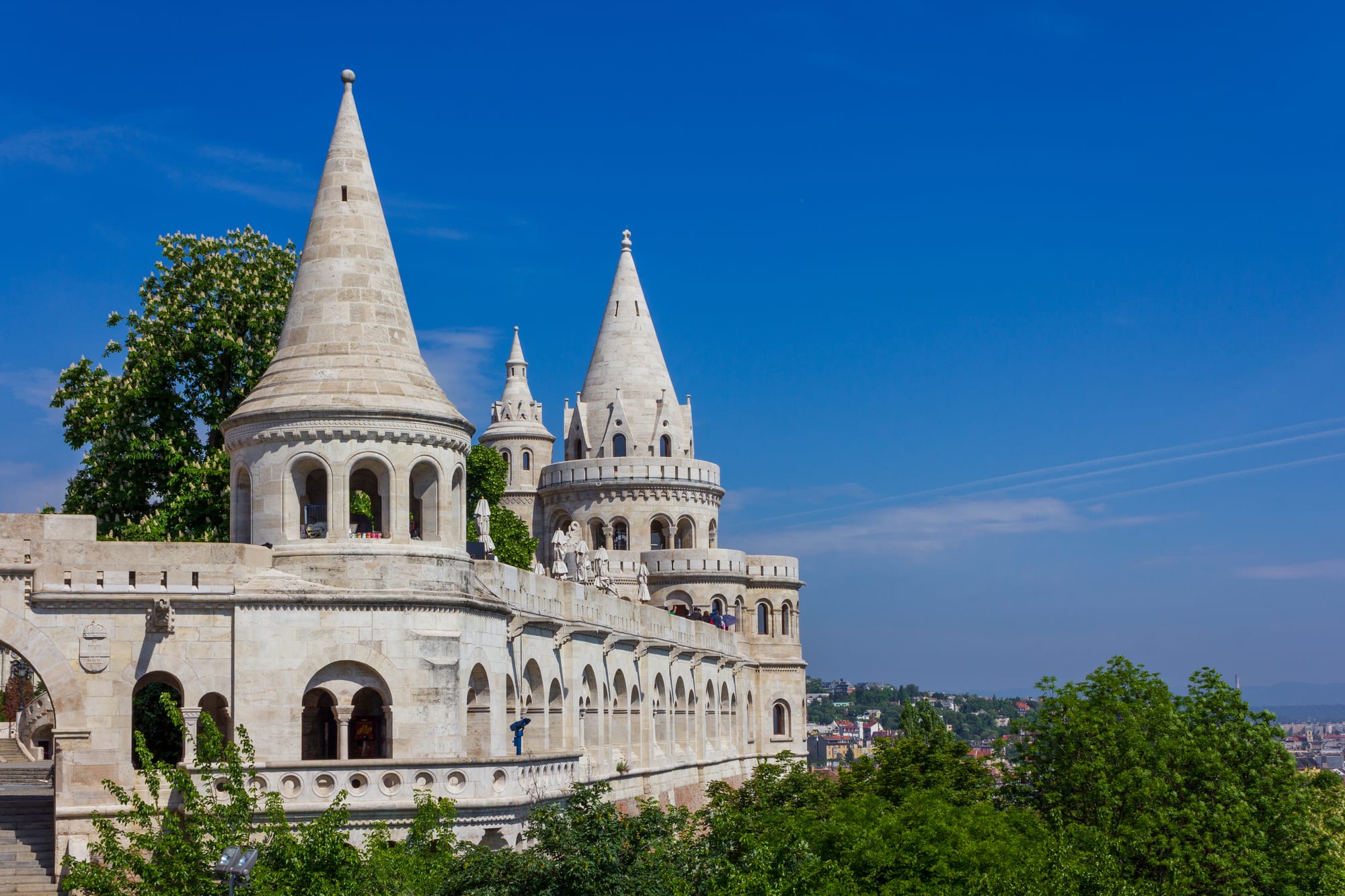 White fairy-tale stone terraces with conical turrets overlooking a city and river