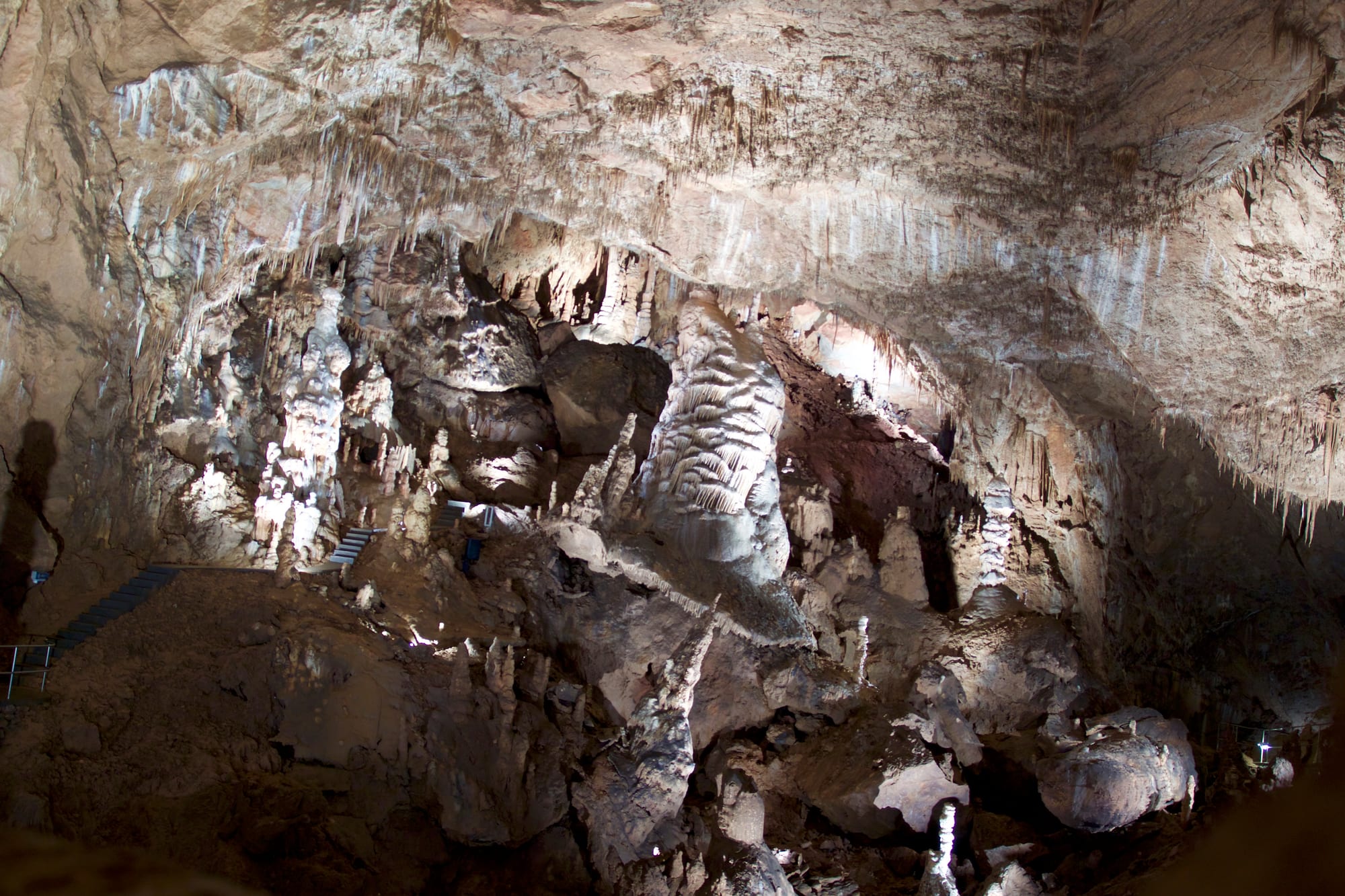 A vast cave chamber with massive stalactite and stalagmite formations, lit for visitors