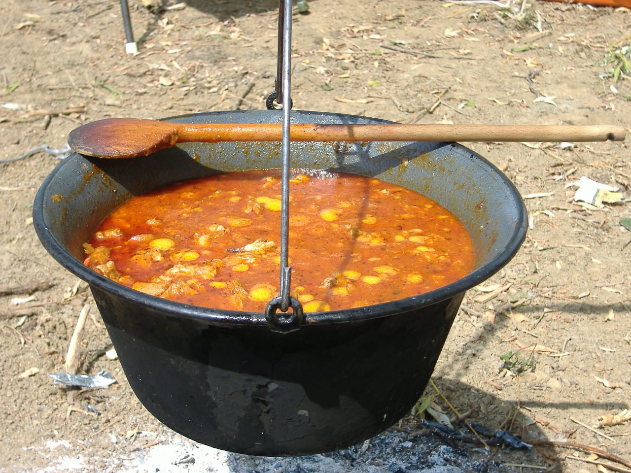A large cauldron of red stew cooking over an open fire