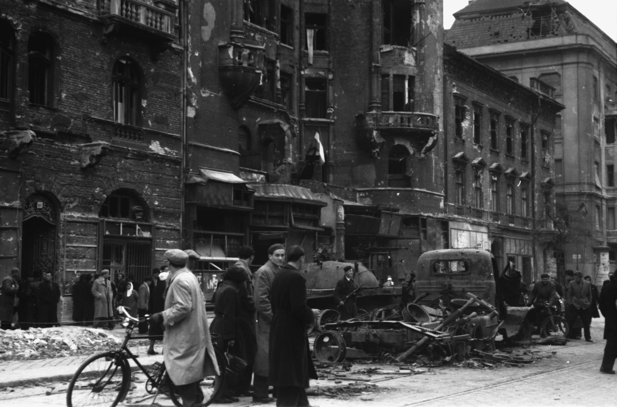 A wrecked tank and truck on a Budapest avenue in 1956, with an armed man and onlookers