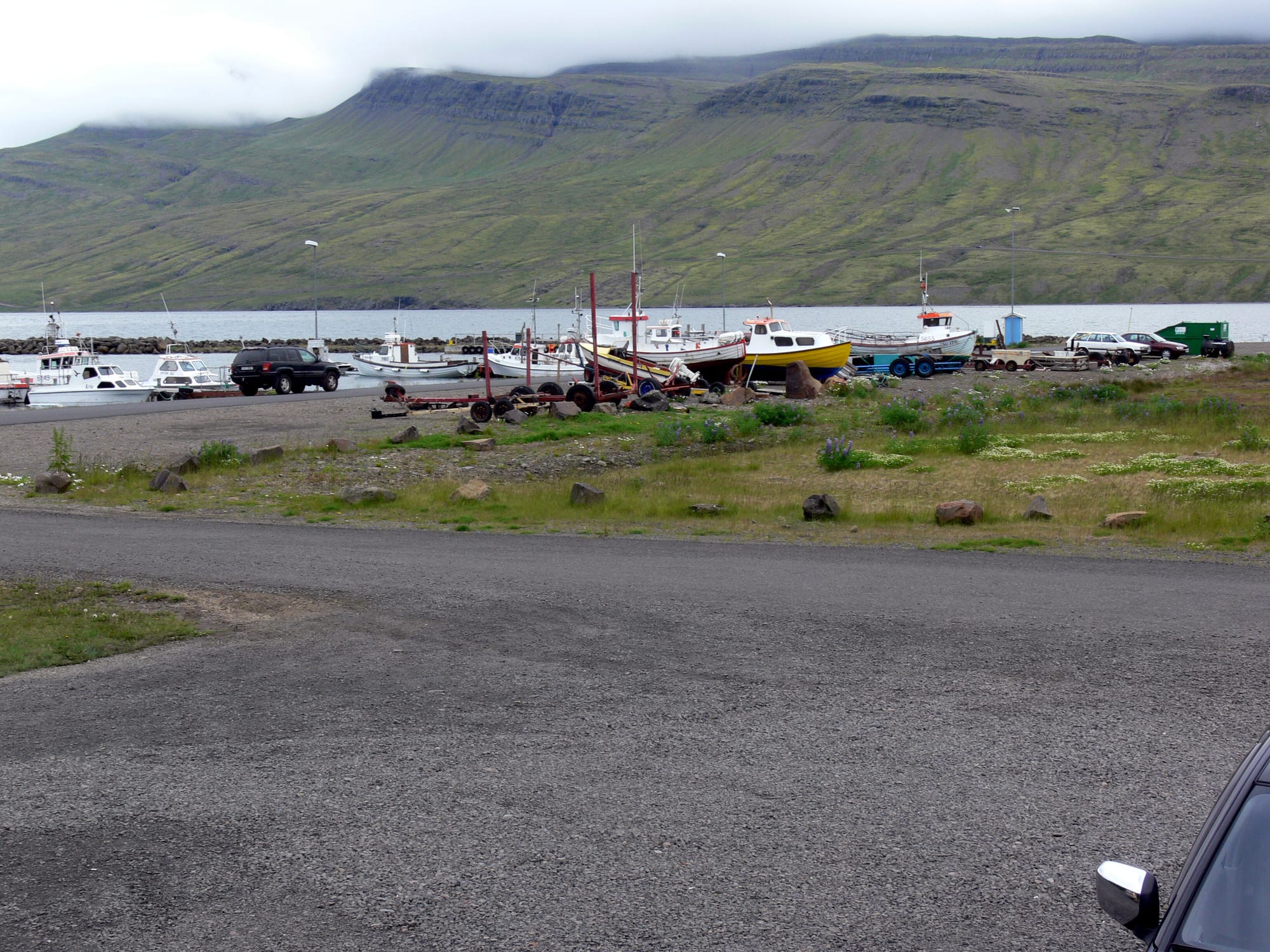 Small fishing boats moored at a harbour in an Icelandic fjord, with steep green mountains rising behind