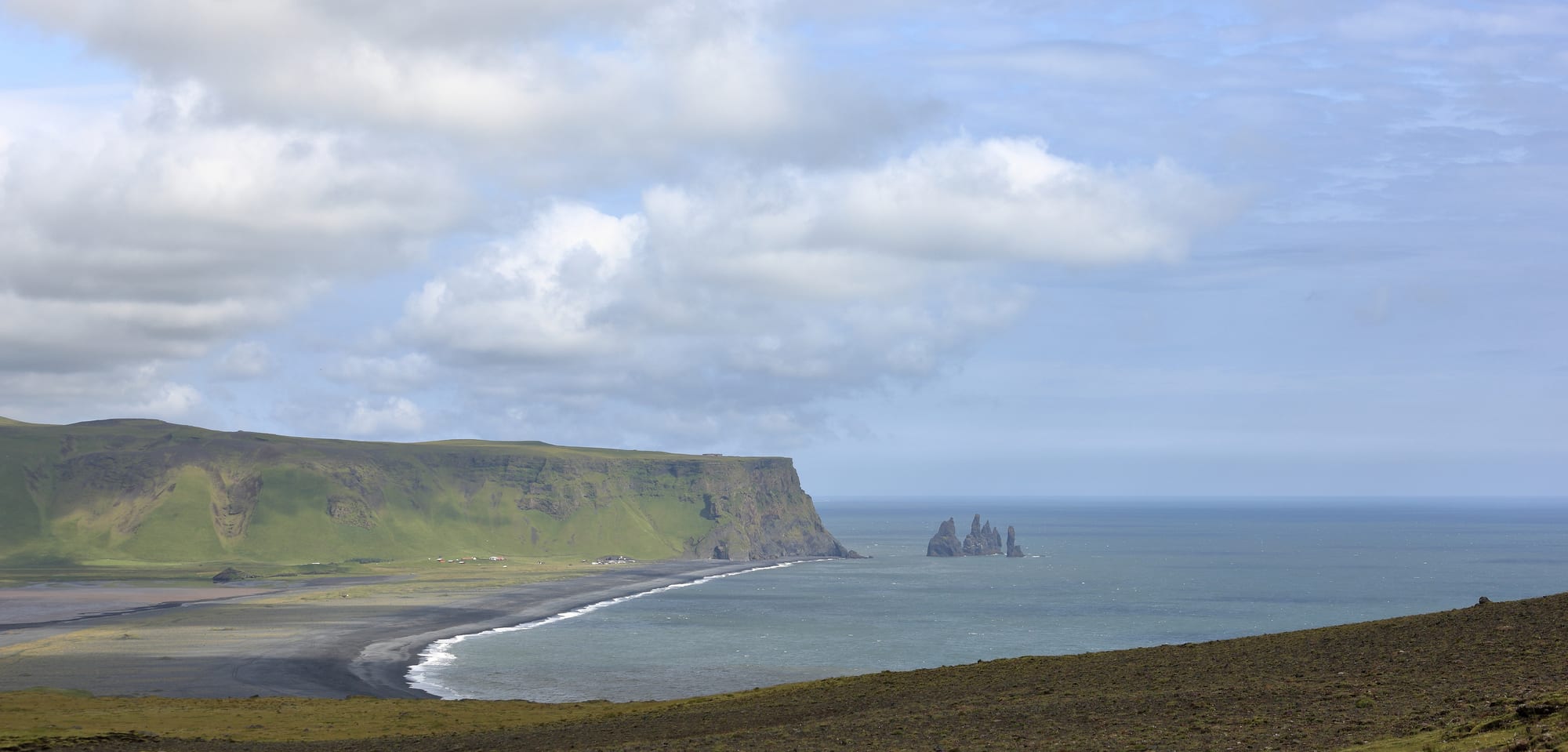 A black-sand beach with basalt sea stacks offshore and columnar cliffs
