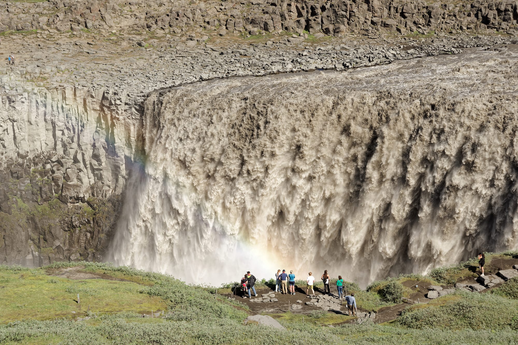 An immense, churning brown waterfall filling a wide canyon with spray