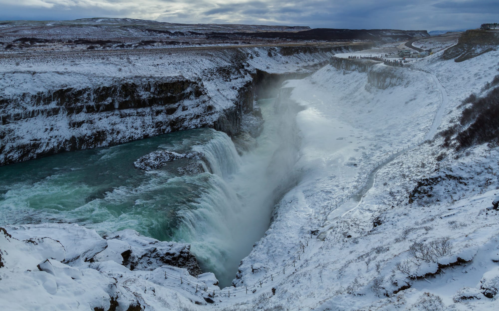 A wide waterfall part-frozen in winter, dropping into a canyon under low light