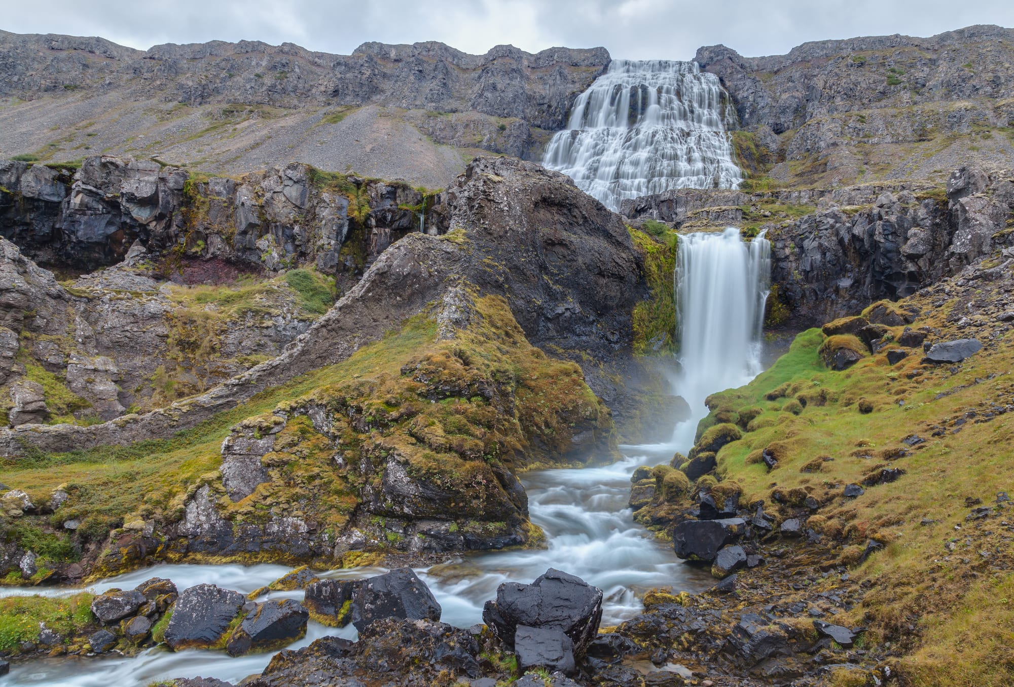 A broad tiered waterfall spilling down a rocky mountainside into smaller cascades