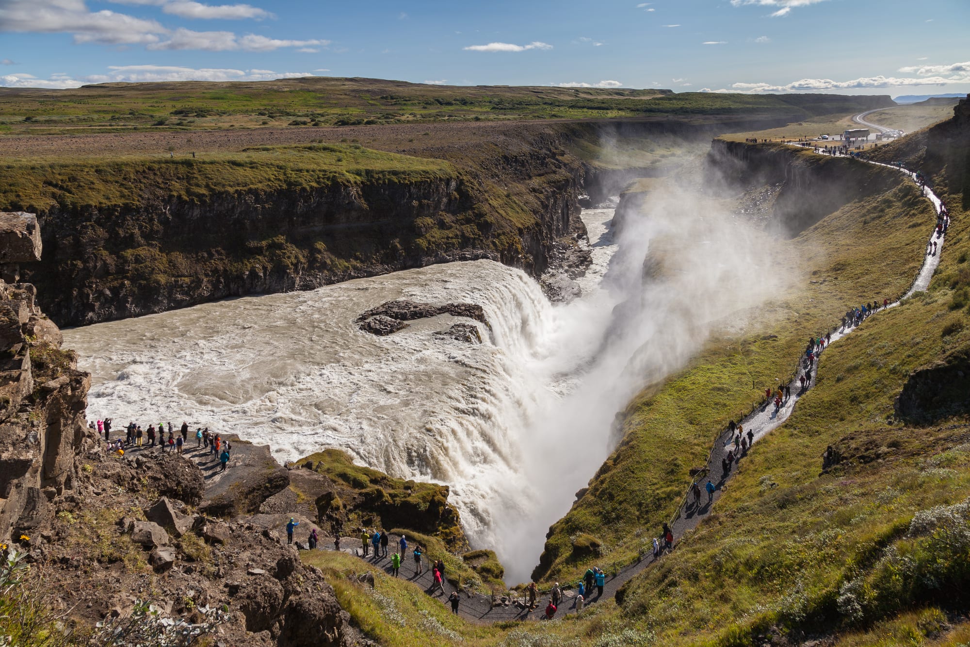 A powerful two-tiered waterfall in a canyon, throwing up spray, with a rainbow