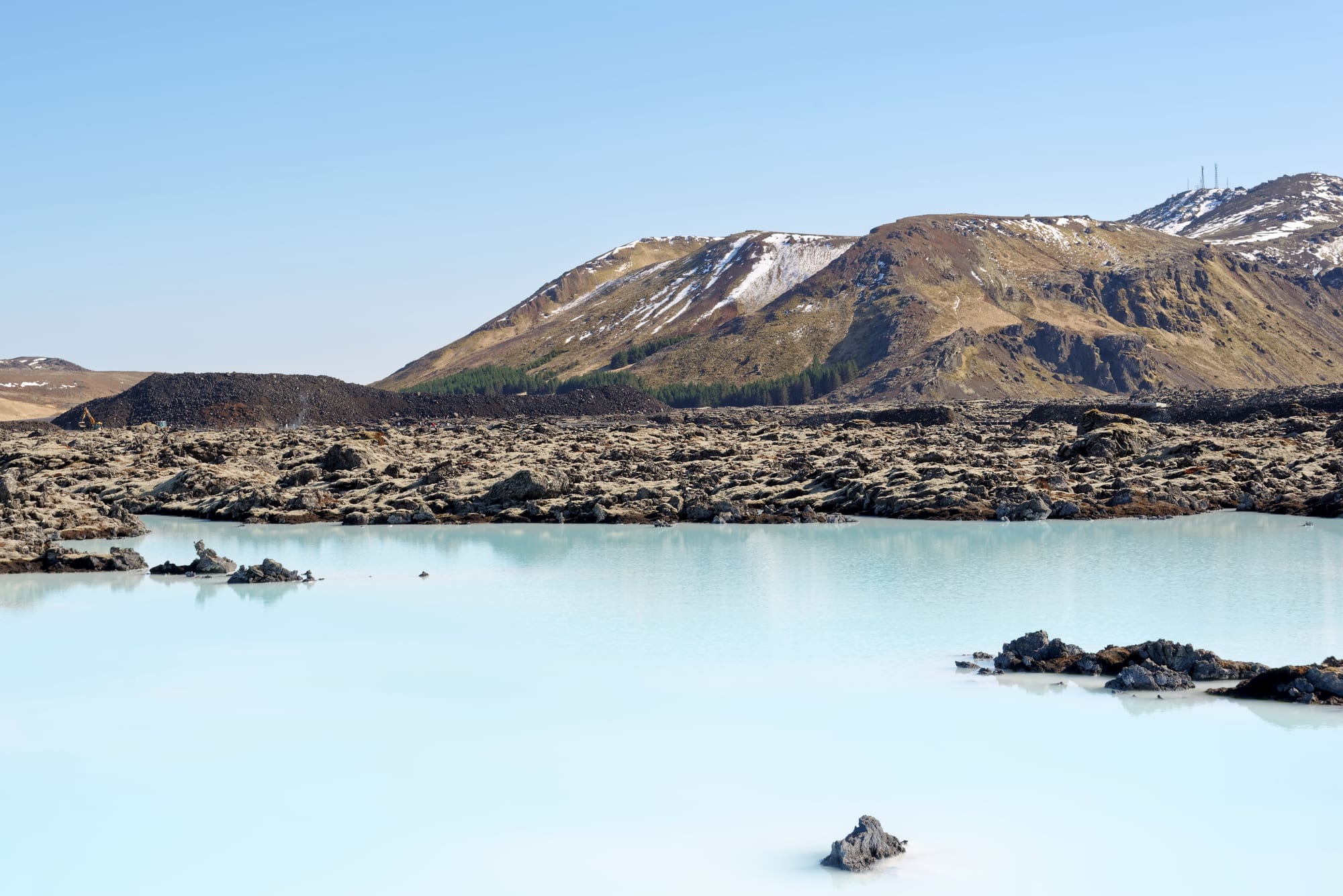 People bathing in a milky pale-blue geothermal pool amid black lava rock