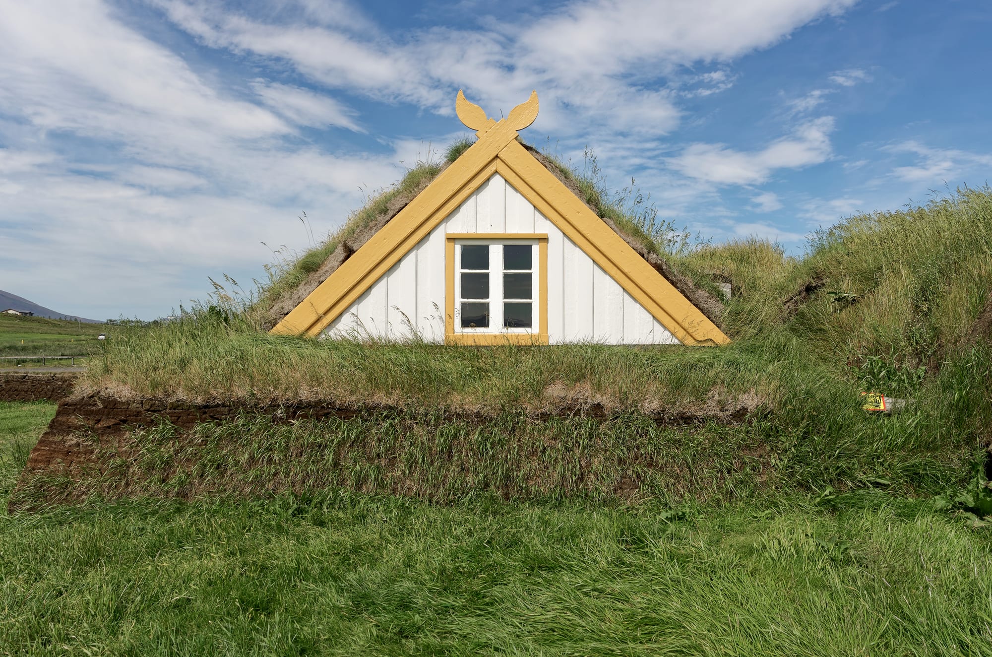 A row of grass-roofed turf farm buildings with white gable ends set into a green slope