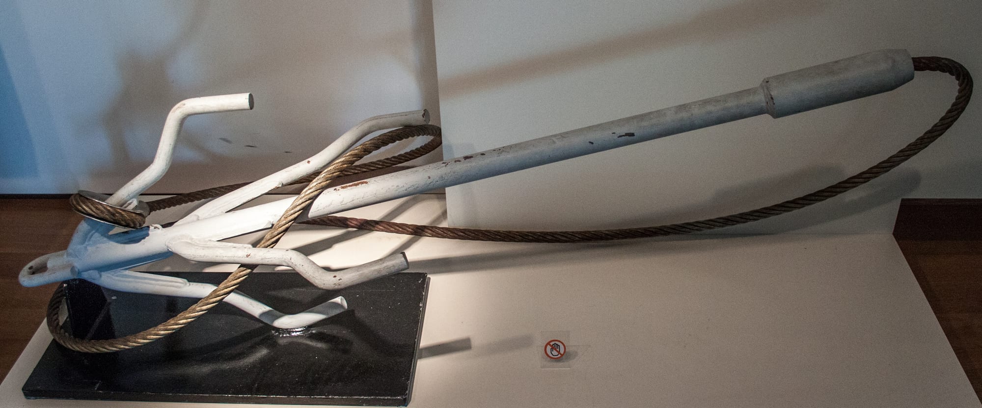 A large steel hooked blade device used to sever trawl cables, displayed on a stand