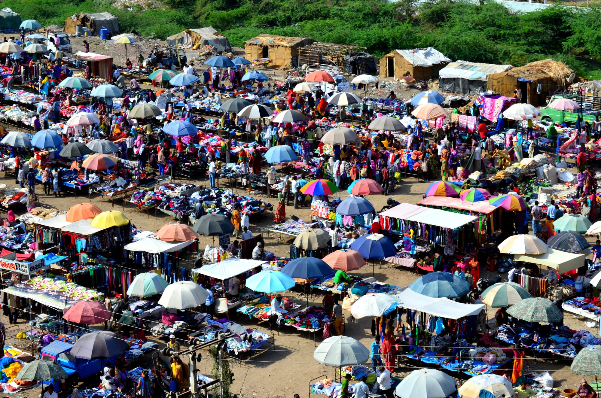 An aerial view of a large open-air market in India, with dozens of colourful umbrella-covered stalls and crowds of shoppers
