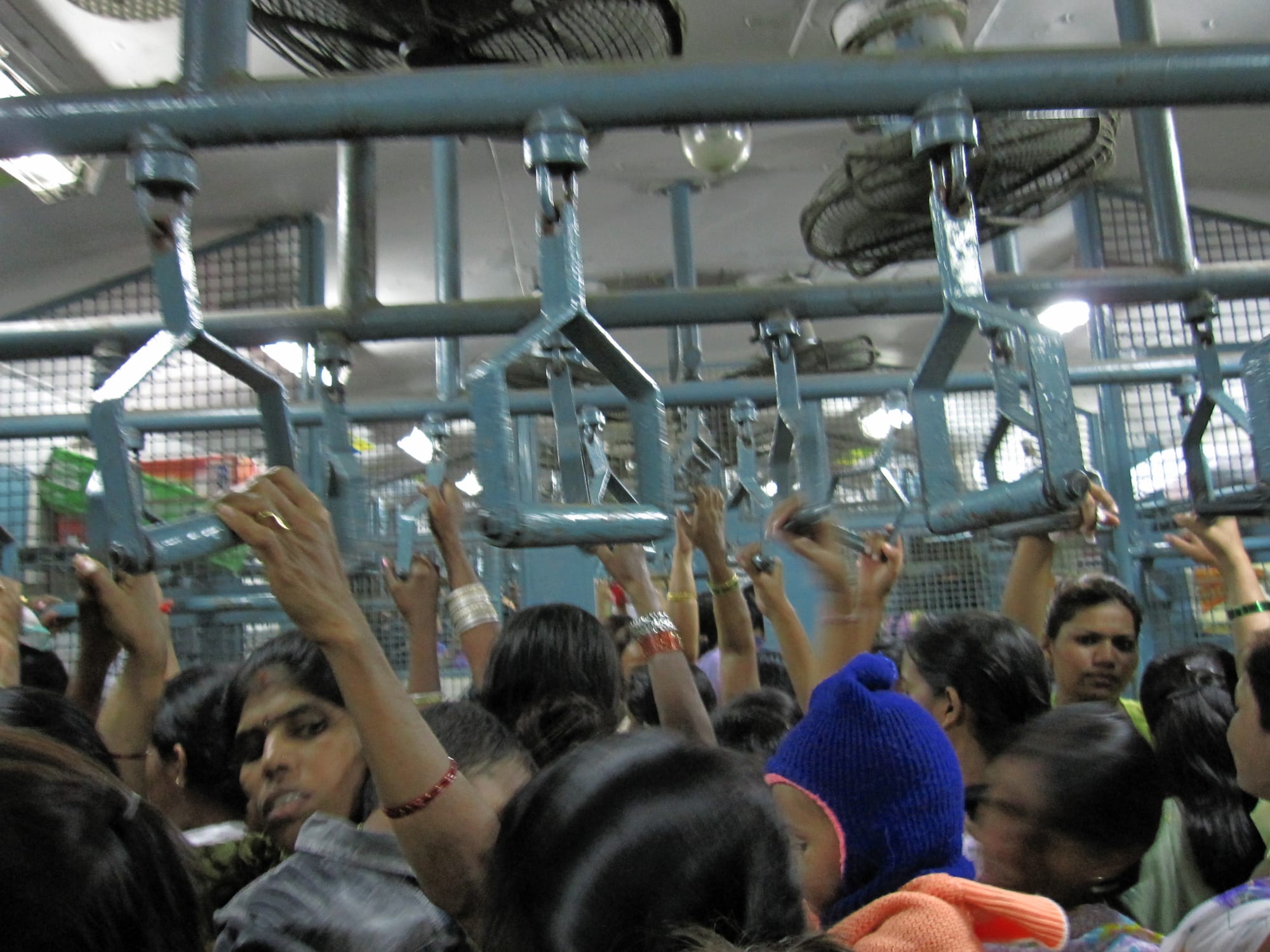 Passengers packed tightly inside a crowded Indian commuter train, holding overhead straps