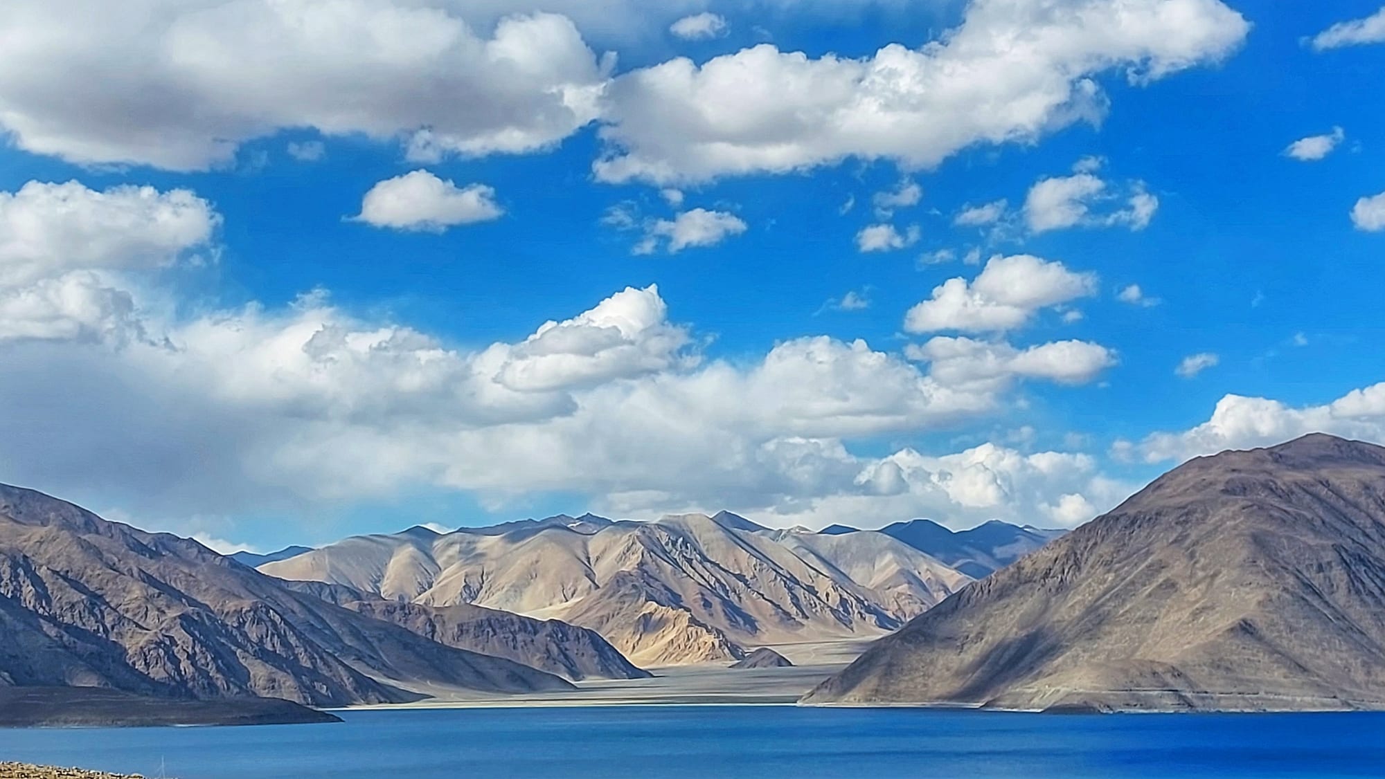 A long, vivid blue lake between stark brown mountains under a deep sky
