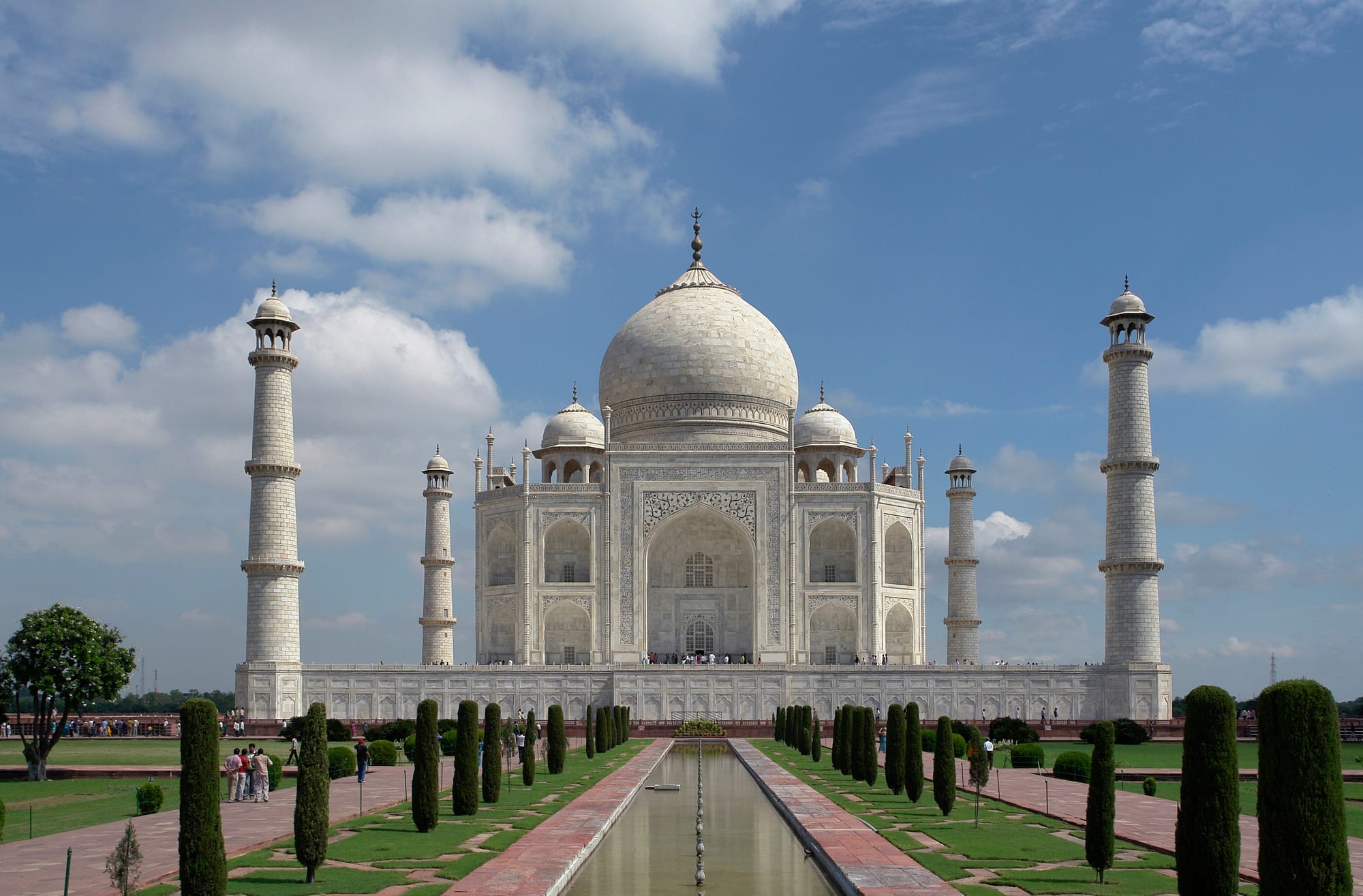 A white domed marble mausoleum with four minarets, perfectly symmetrical, reflected in a long pool