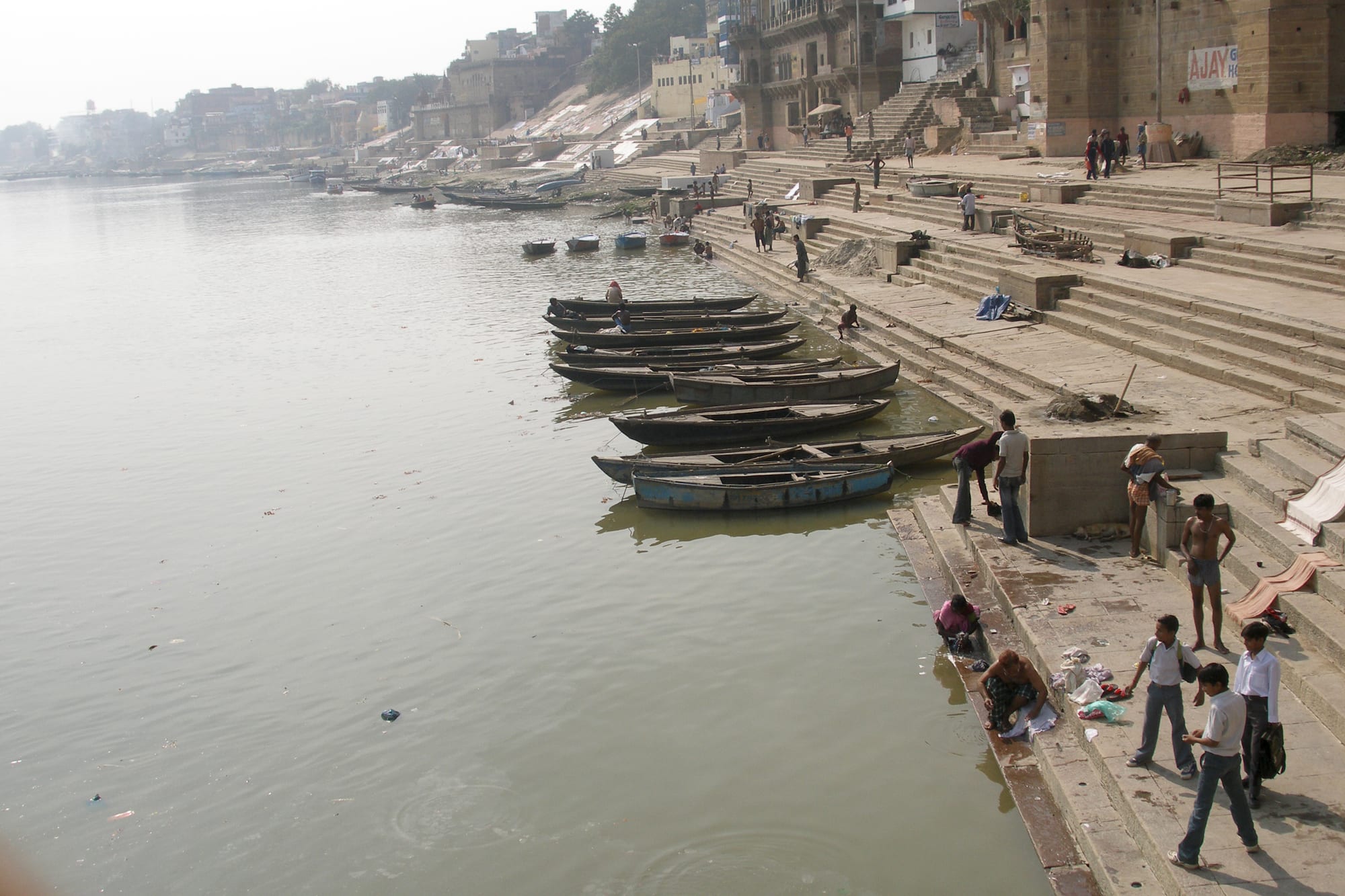 Crowded riverside steps and tall old buildings along the Ganges at dawn, boats on the water
