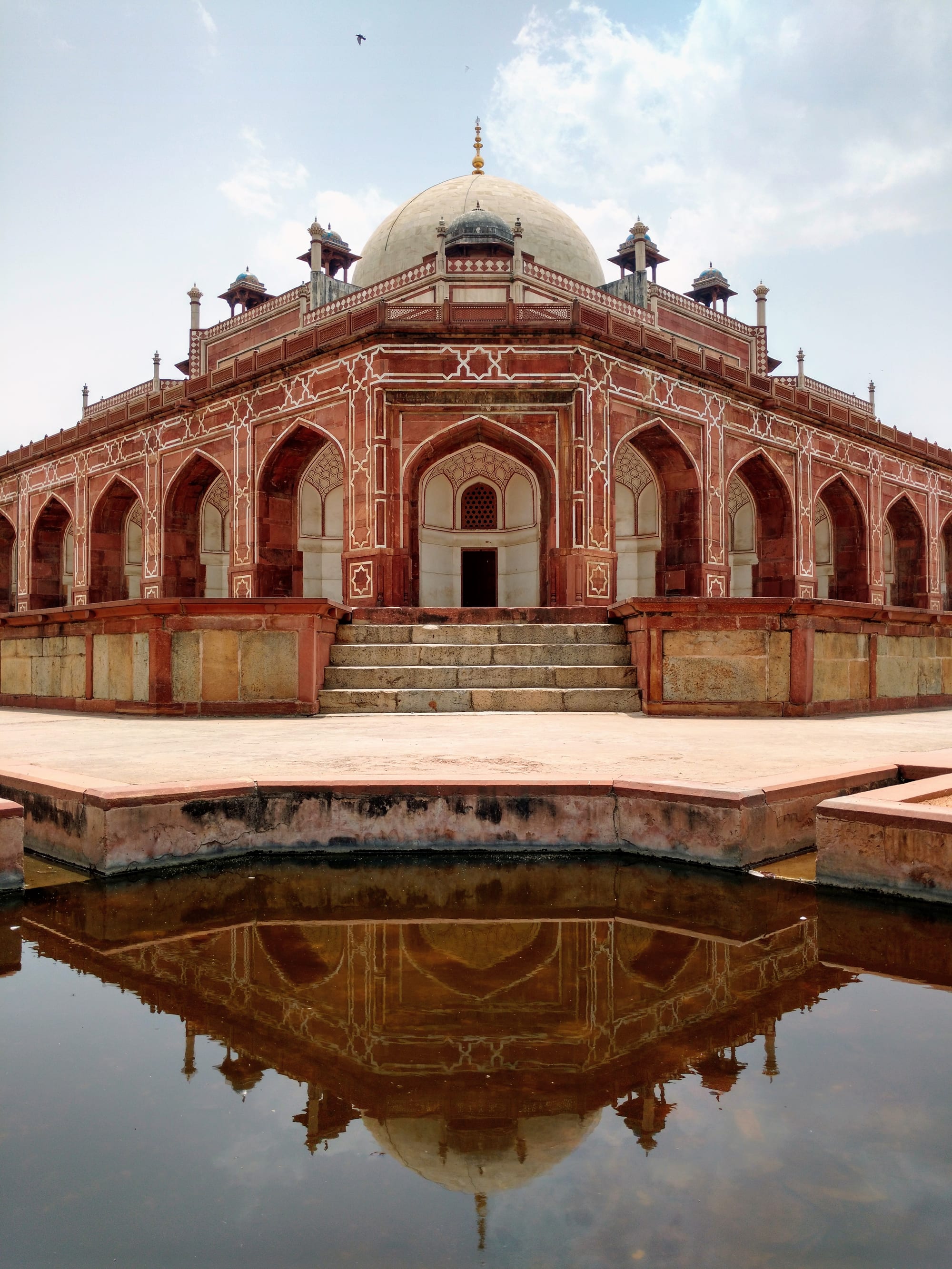 A large red sandstone and white marble Mughal tomb with a bulbous dome, in formal gardens