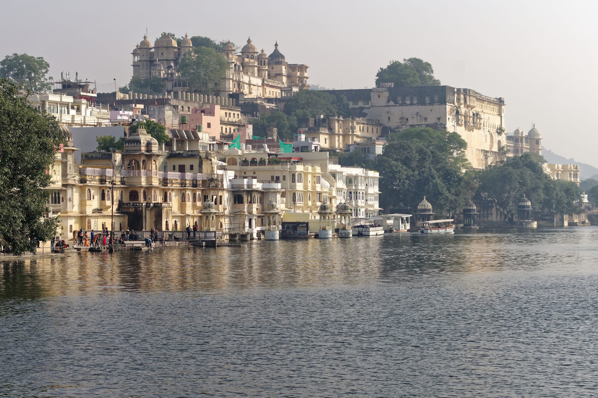 A white palace complex along the edge of a calm lake, with island palaces and hills behind