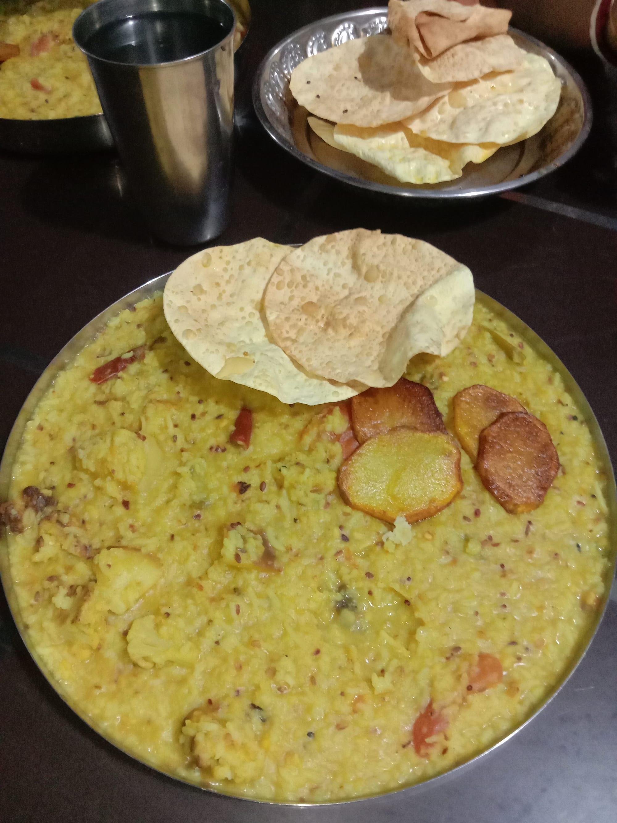 A bowl of soft yellow rice and lentils with a crisp papad on the side
