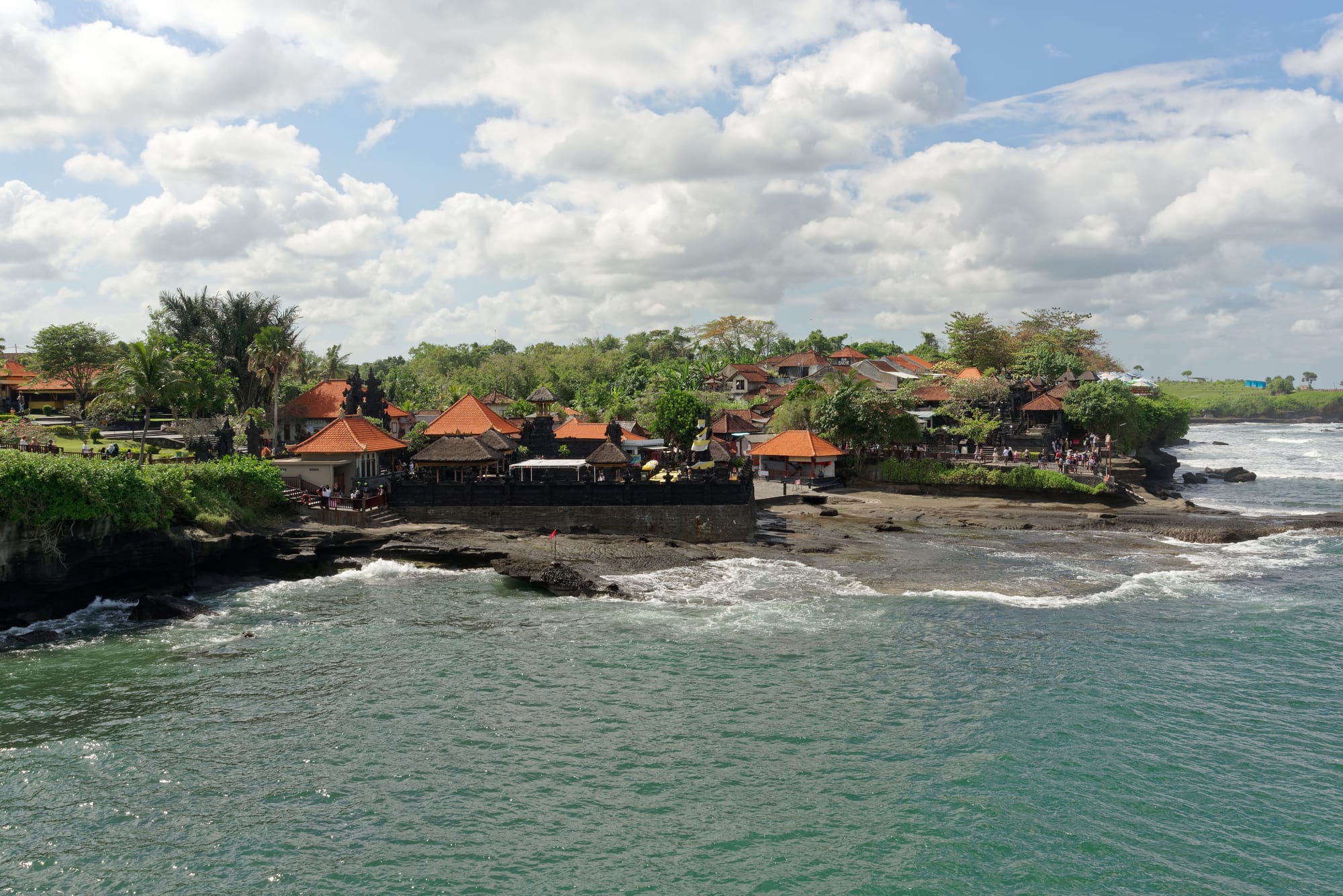 A small temple on a rock stack just offshore, waves breaking around its base