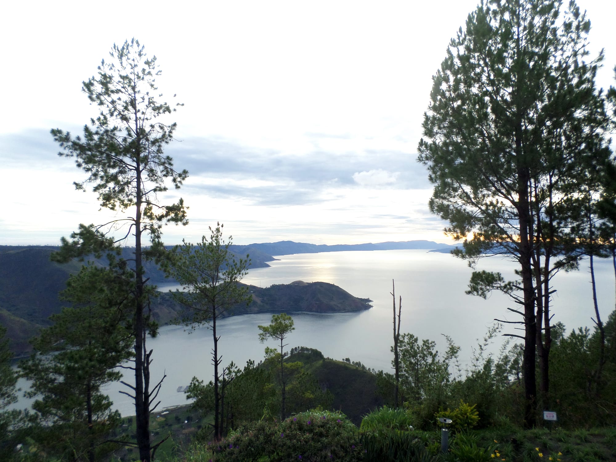 A vast blue lake with a large island in the middle, ringed by green highland ridges