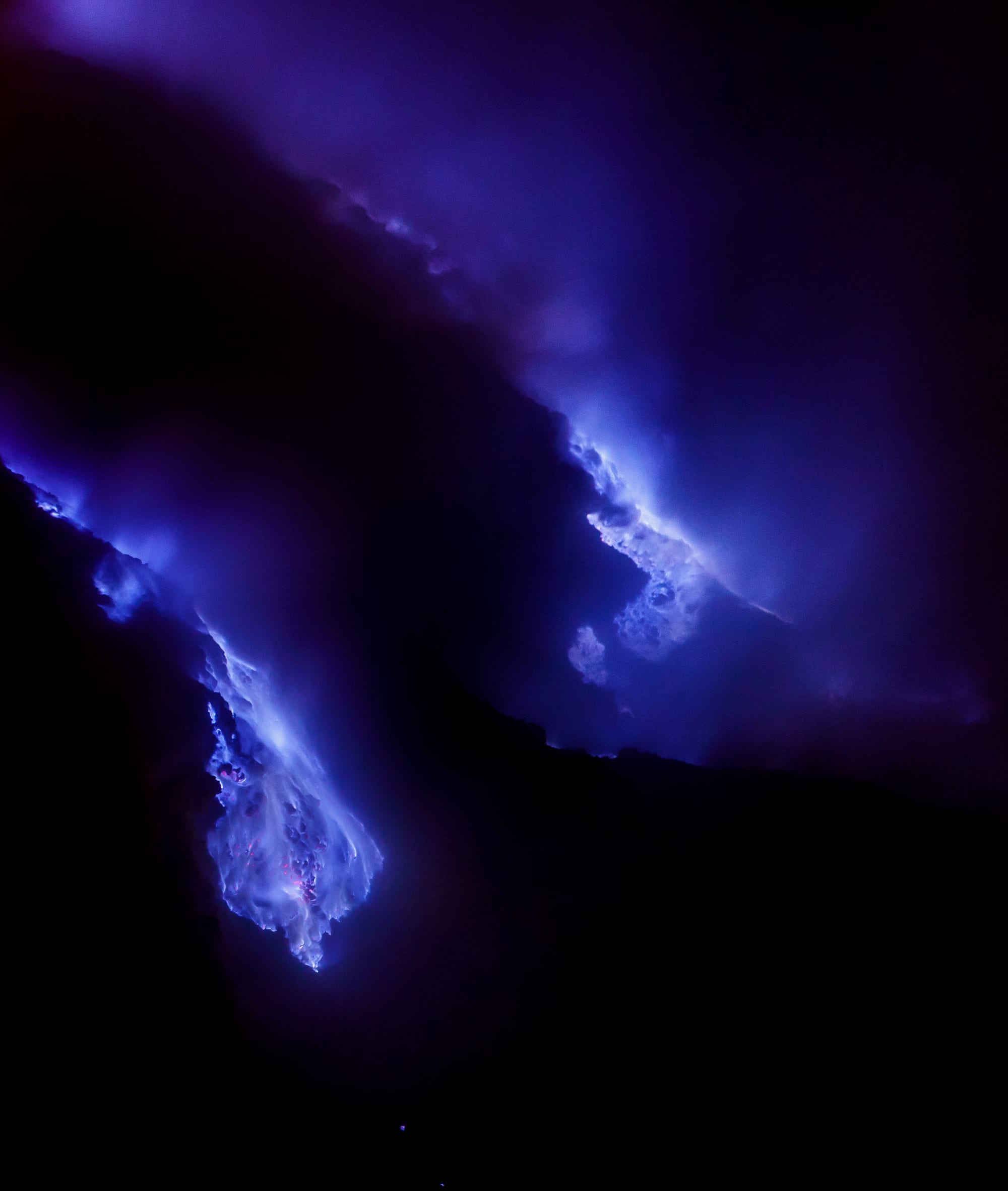 Electric-blue flames burning among rocks in the darkness of a volcanic crater