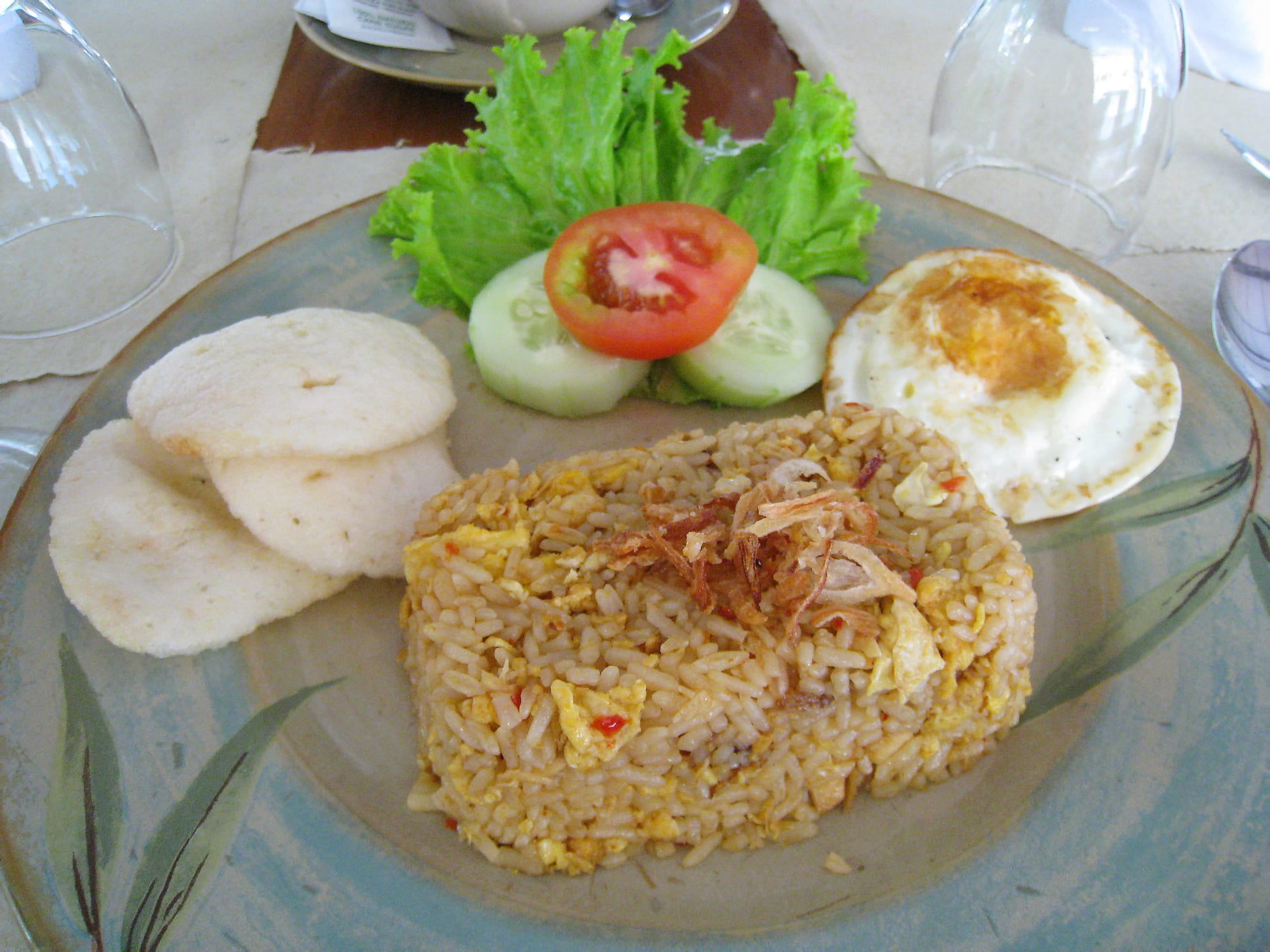 A plate of fried rice topped with a fried egg, served with crackers and fresh vegetables