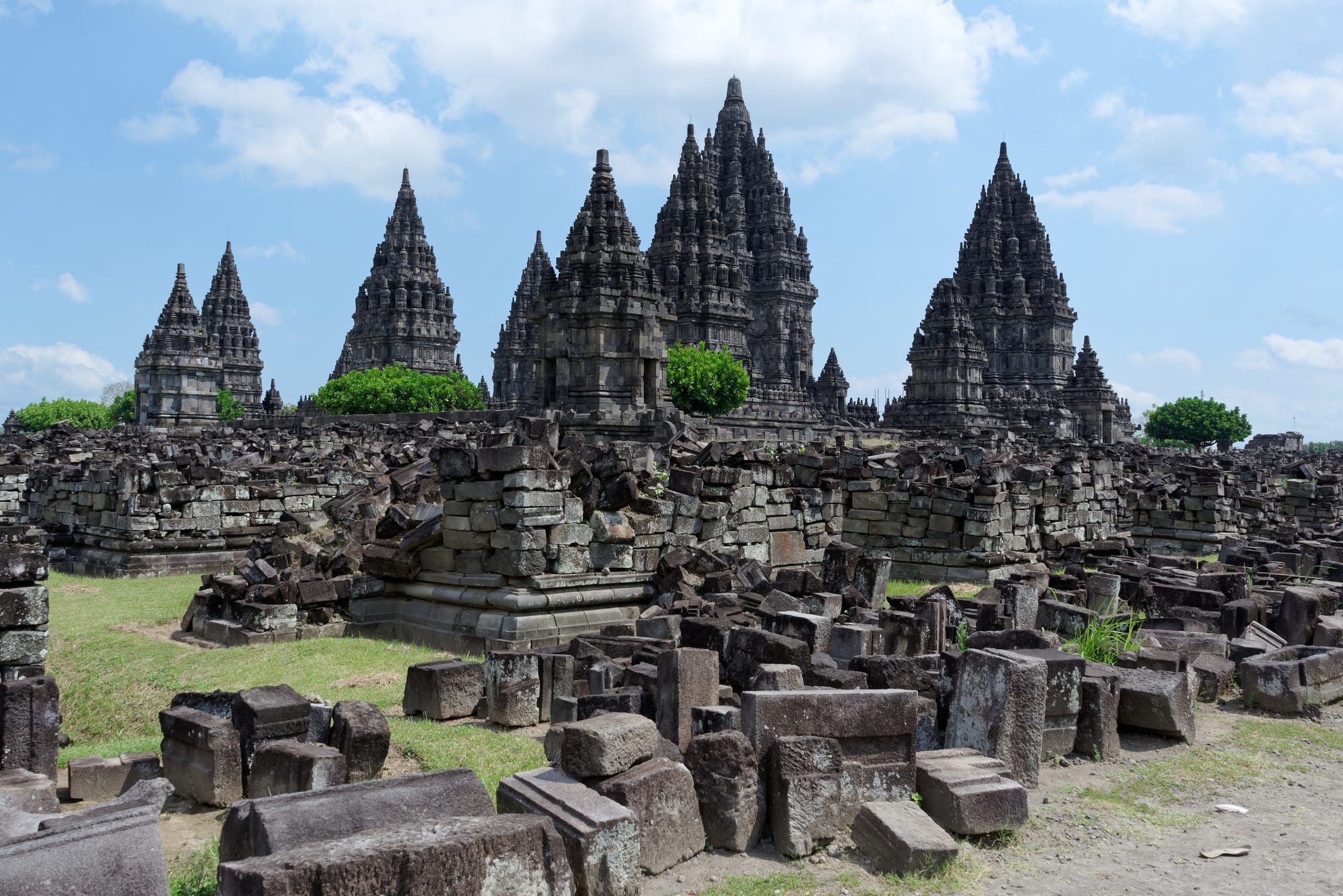 A cluster of tall, sharply pointed stone Hindu temple towers rising above a green plain