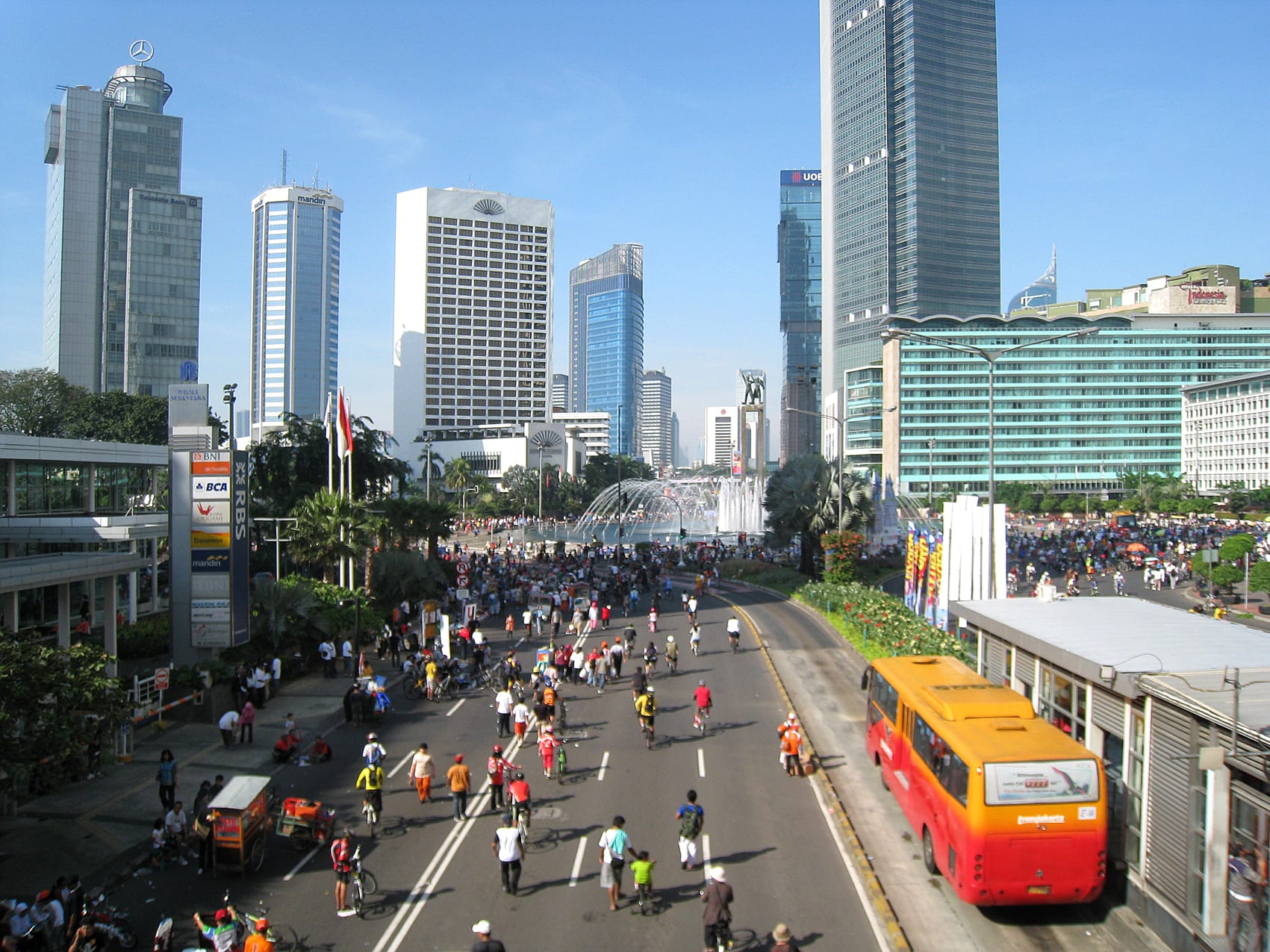 Crowds of pedestrians and cyclists filling a wide avenue beneath Jakarta's high-rise towers