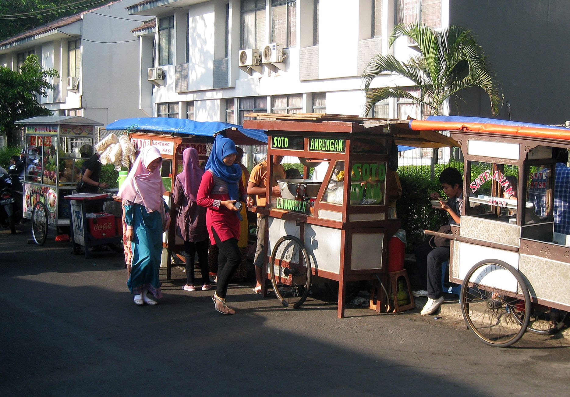 A row of mobile food carts, or kaki lima, on a Jakarta street with customers buying food