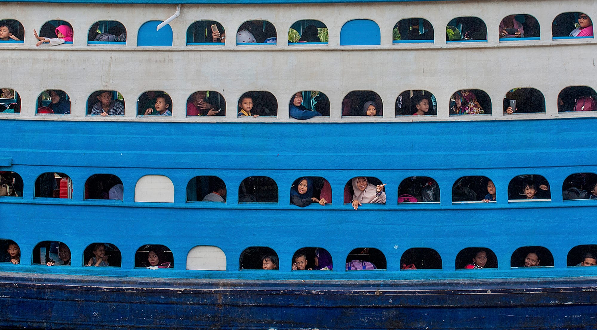 Passengers looking out from multiple stacked decks of a crowded ferry during Indonesia's mudik homecoming travel