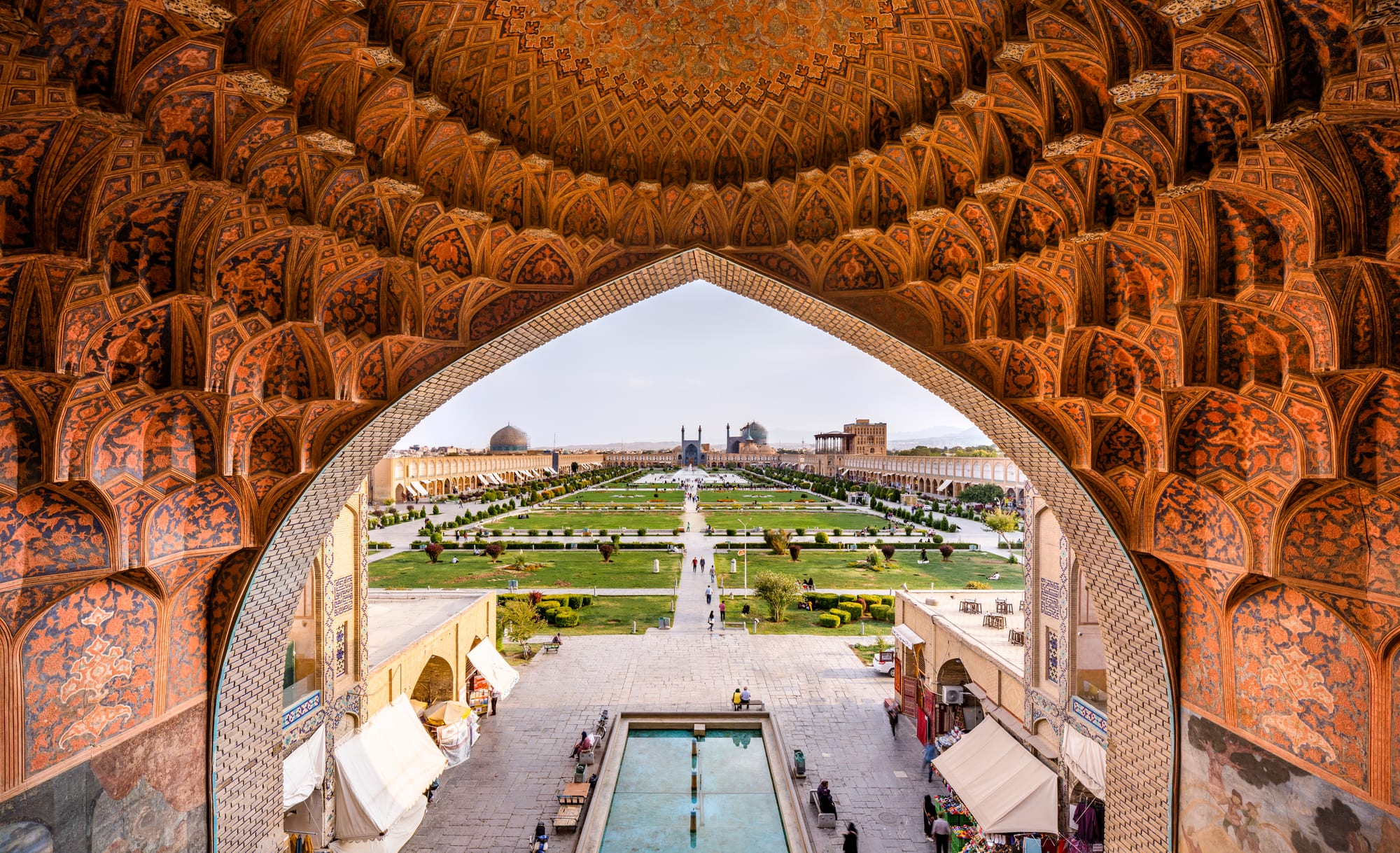A vast rectangular plaza framed by arcades, a blue-domed mosque at one end and a palace at the side