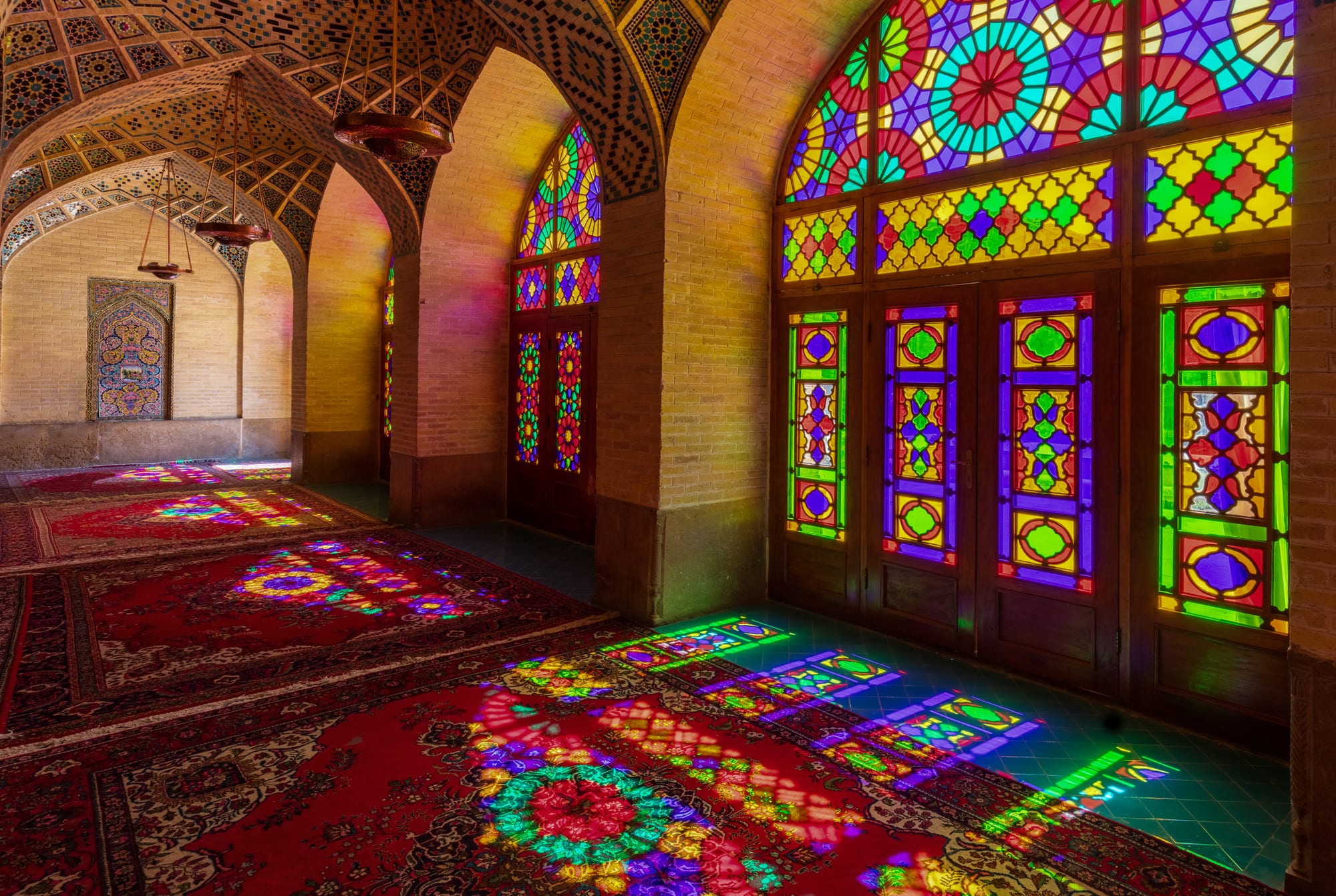 A columned prayer hall where morning sun through stained glass throws pools of coloured light across carpets