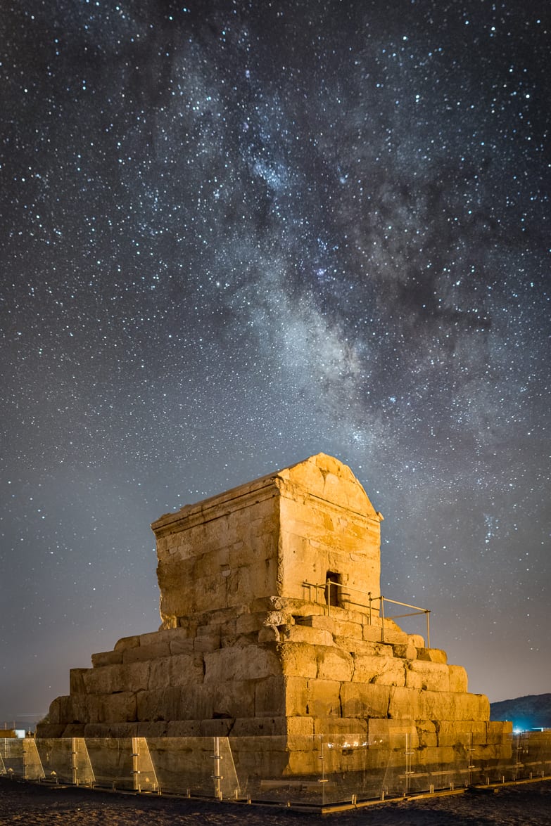 A simple stepped stone tomb like a small gabled house on a six-tiered base, alone in a plain