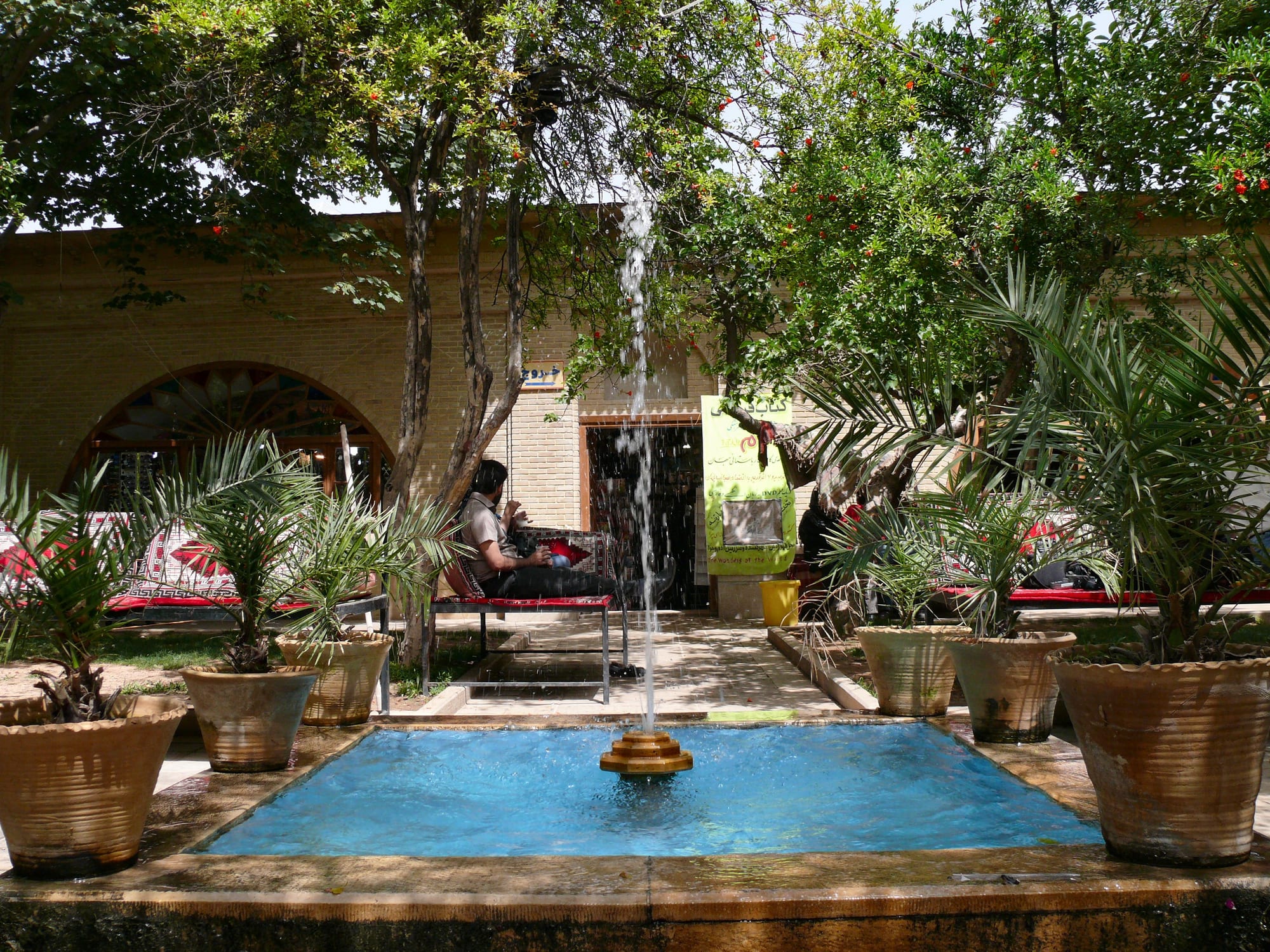 A man reclining on a traditional bench seat beside a fountain in a shaded garden tea house