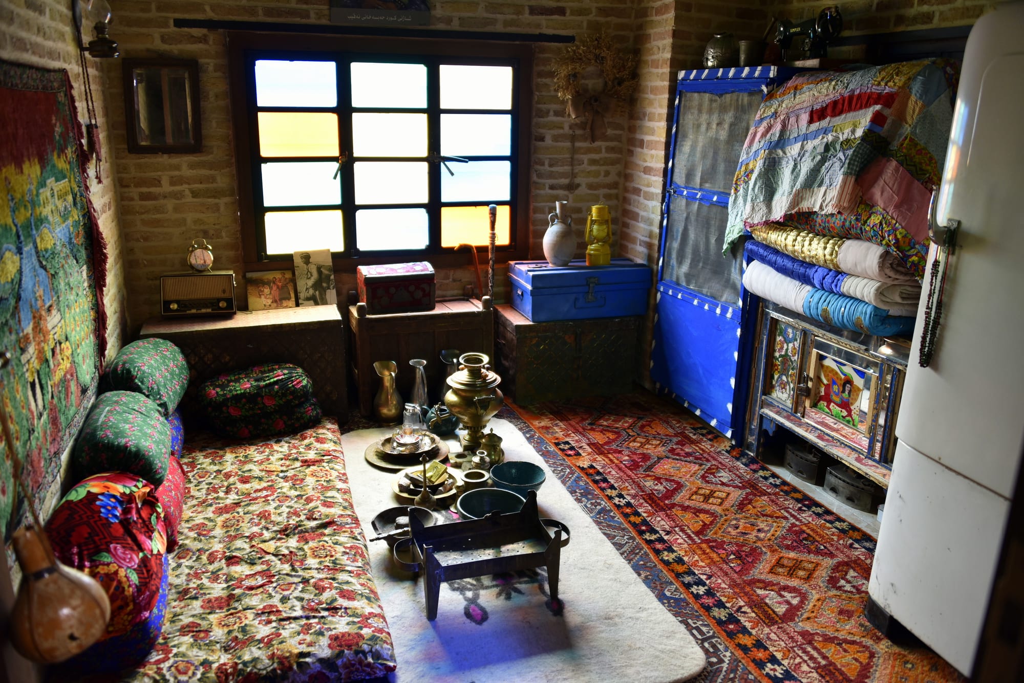 A traditional low-seating living room with patterned cushions, a brass tea tray and layered carpets