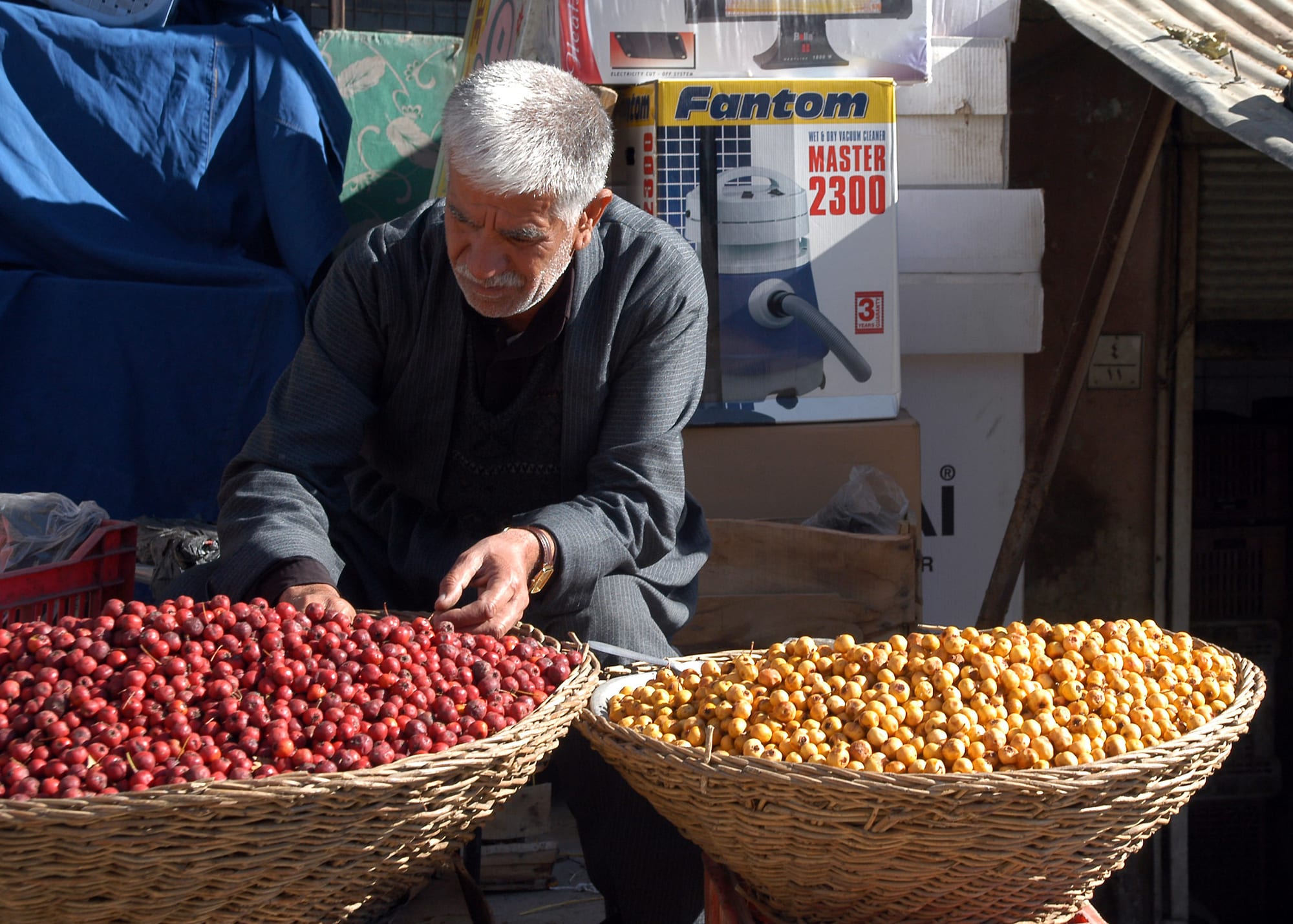 A vendor arranging baskets of red and yellow berries at a market stall