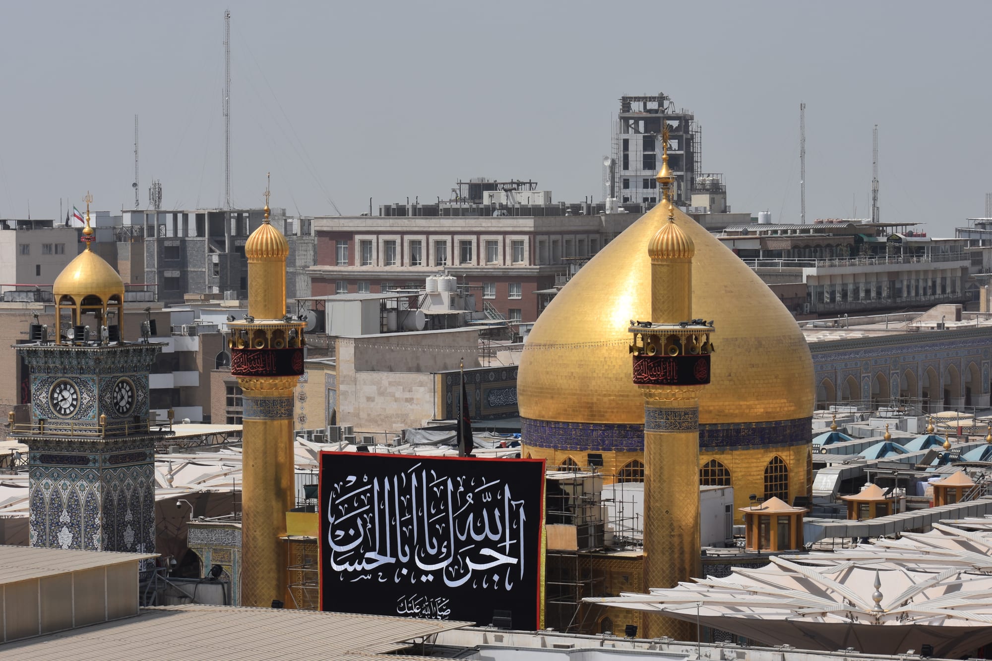 A large mosque with a brilliant gold dome and two gold minarets above a crowded courtyard