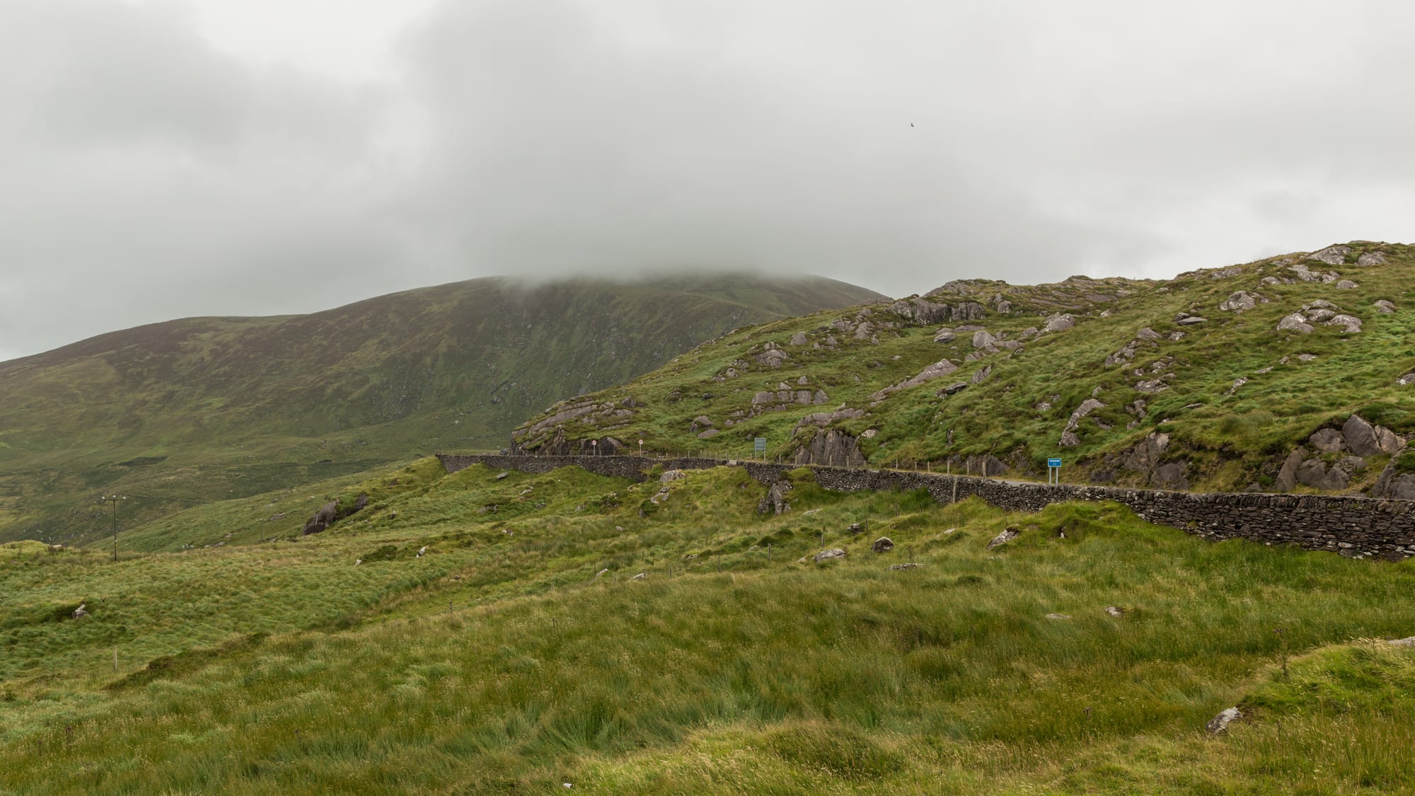 A winding coastal road above a bay ringed by green mountains and islands