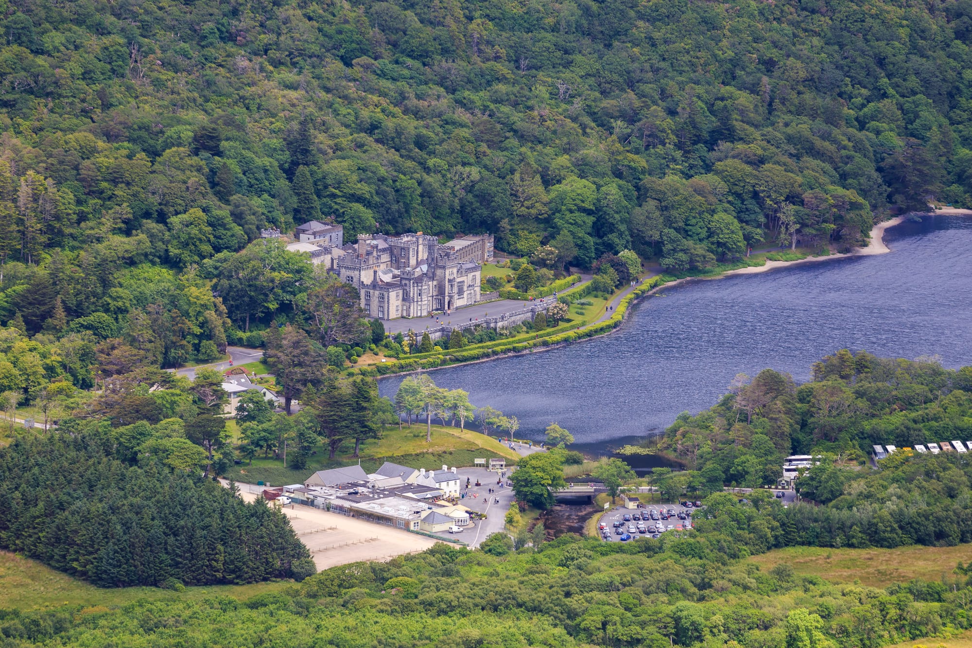 A grey Gothic-revival castle-abbey on a lakeshore backed by a forested mountain